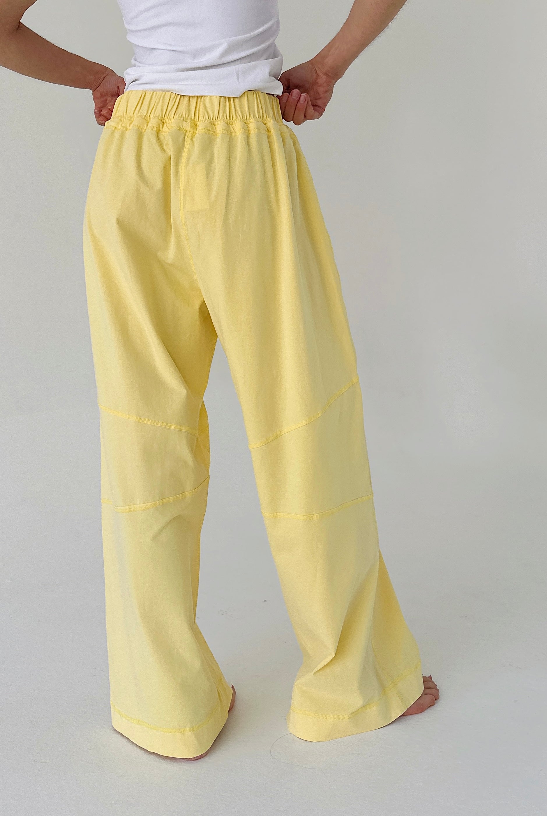Person wearing yellow pants and a white shirt on a plain background from back