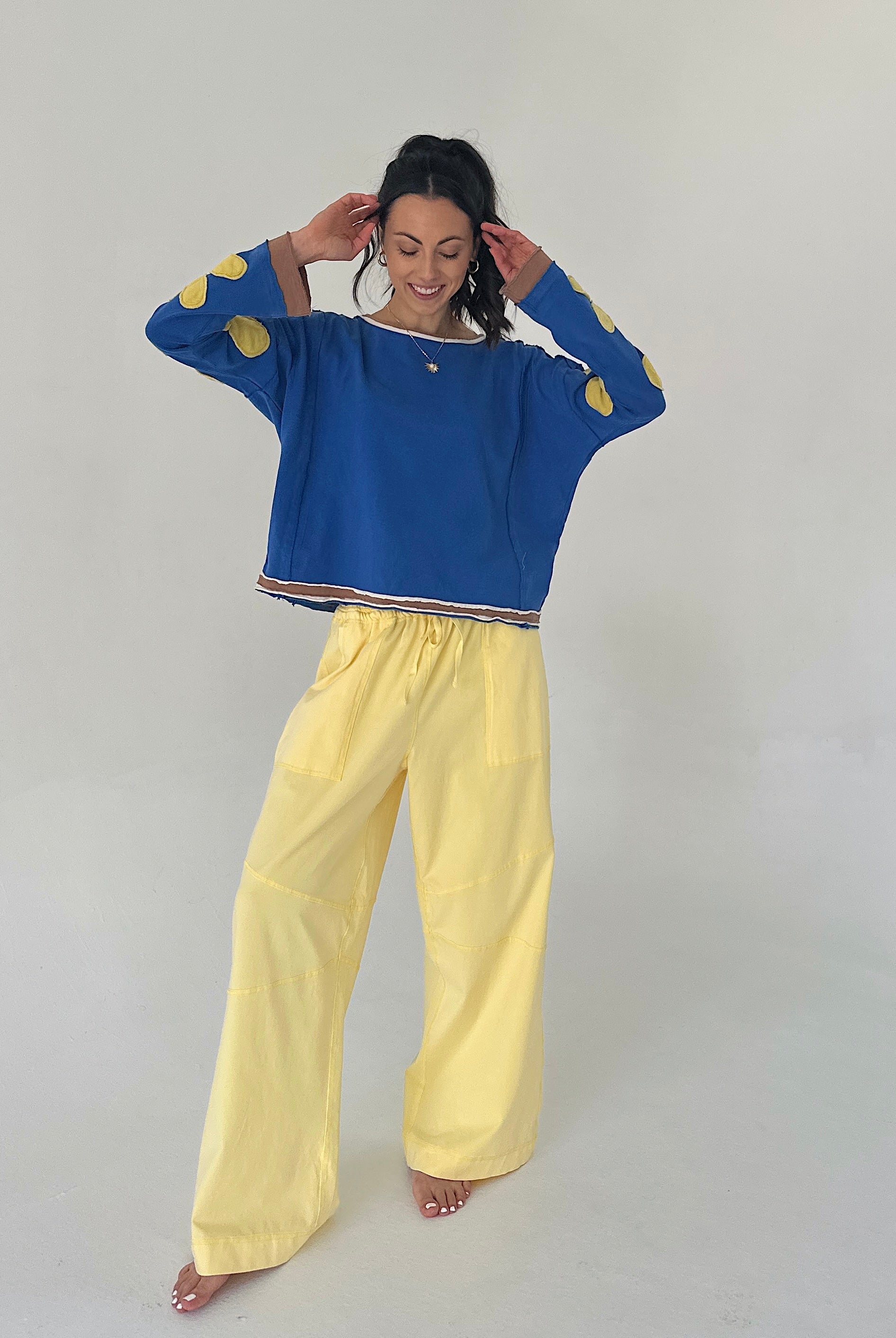Woman wearing a blue sweater with gold accents and yellow pants on a plain background