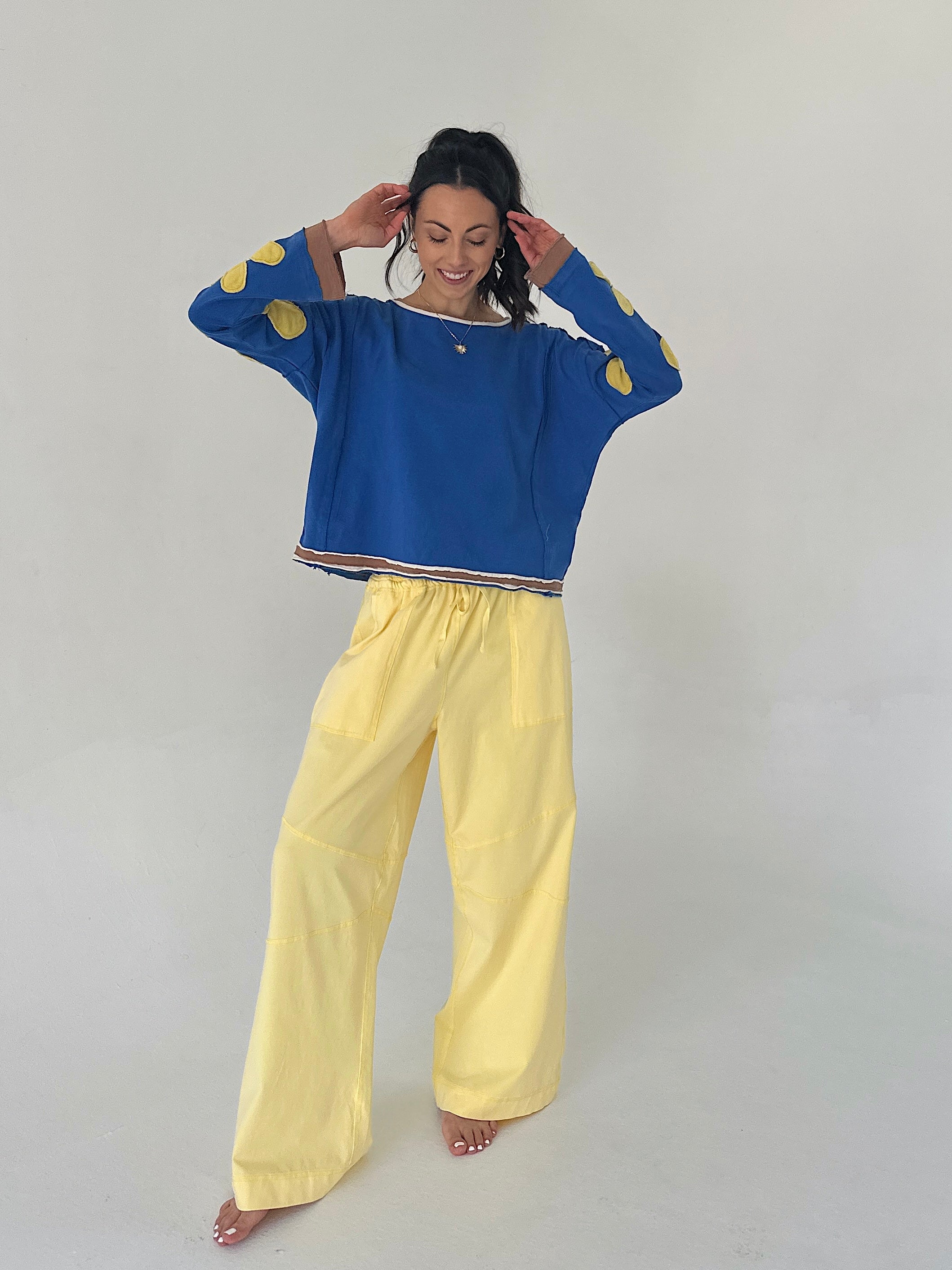 Woman wearing a blue sweater with gold accents and yellow pants on a plain background