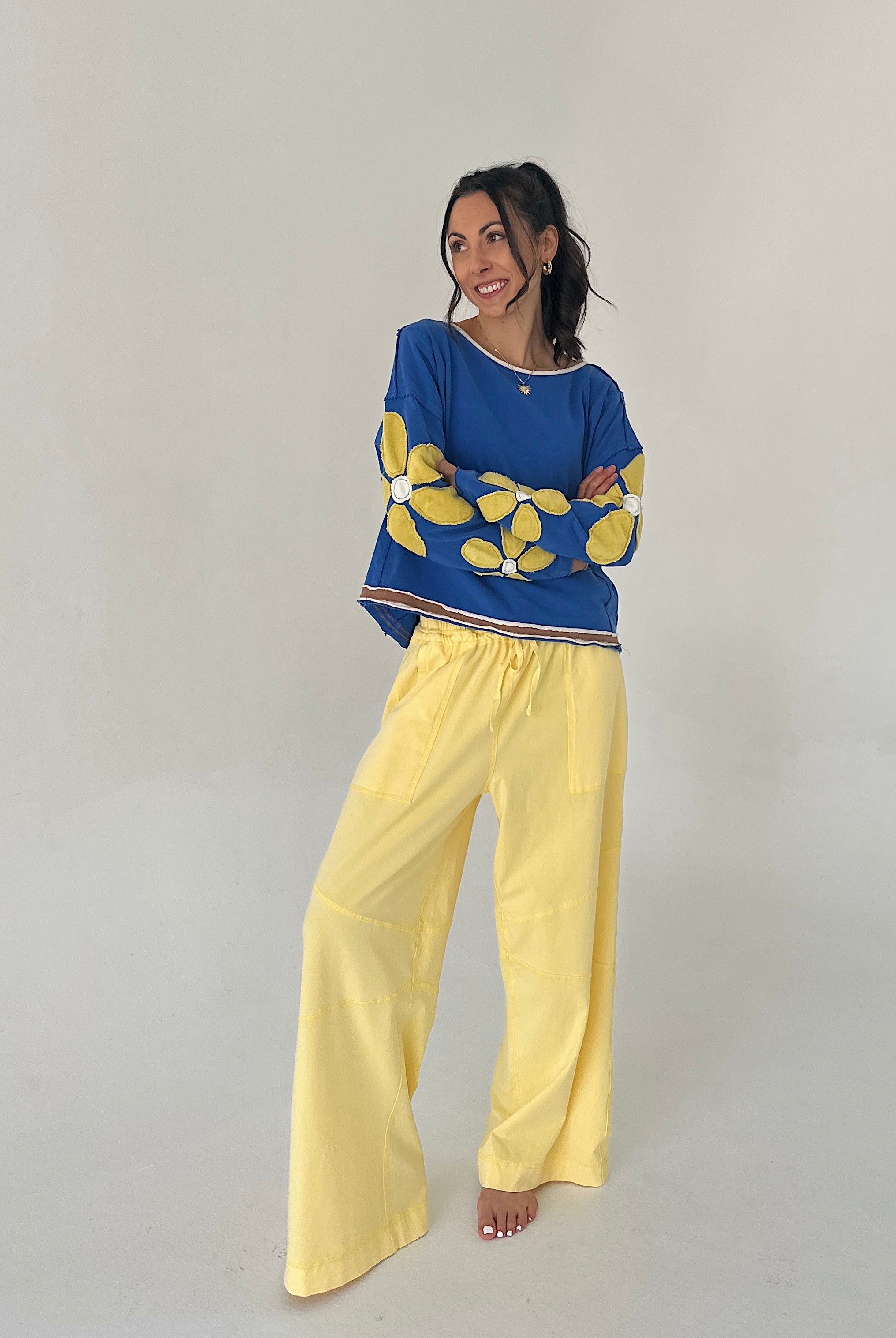 Woman wearing a blue sweater with yellow floral patterns and yellow pants on a plain background