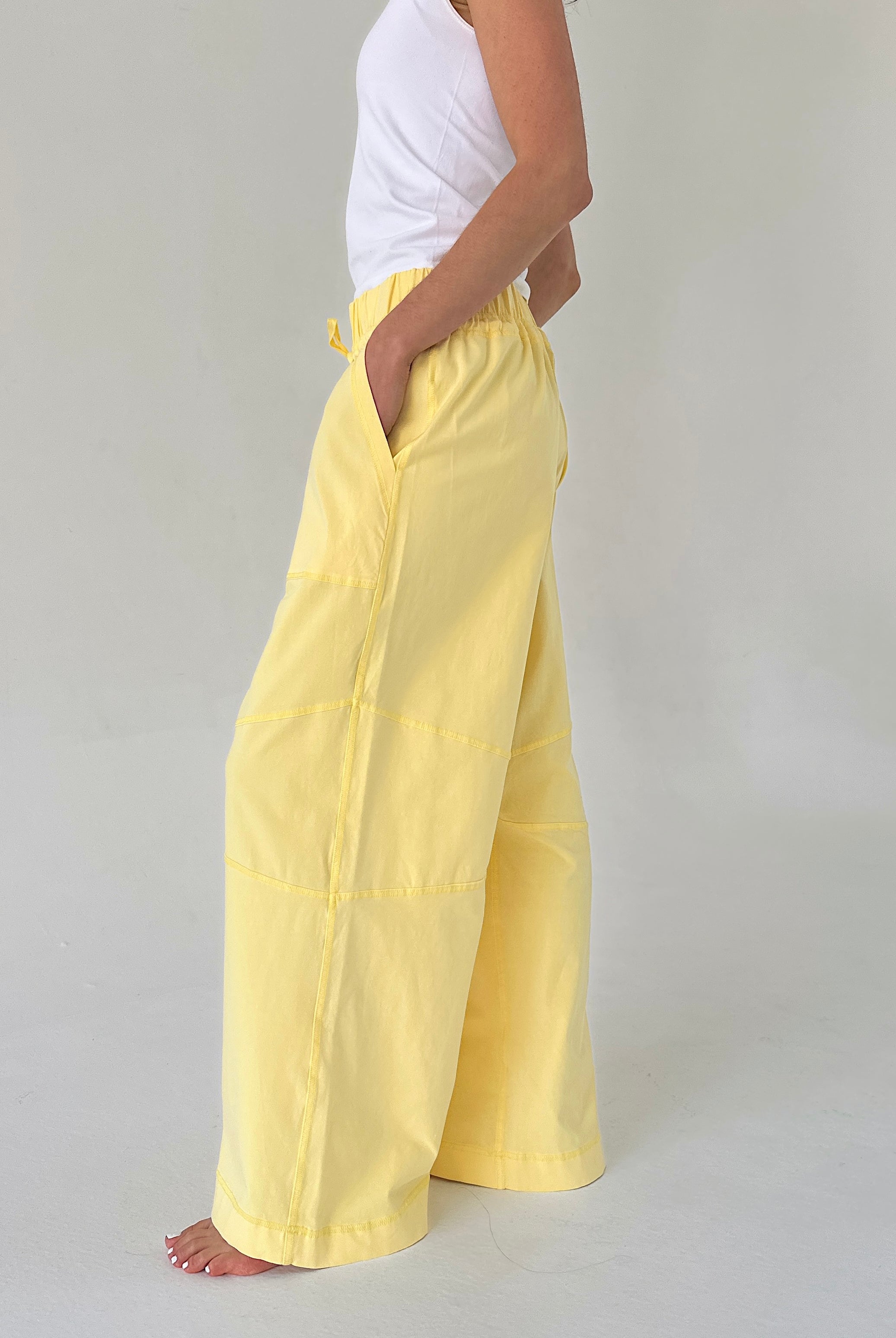 Person wearing yellow pants and a white top on a plain background from side