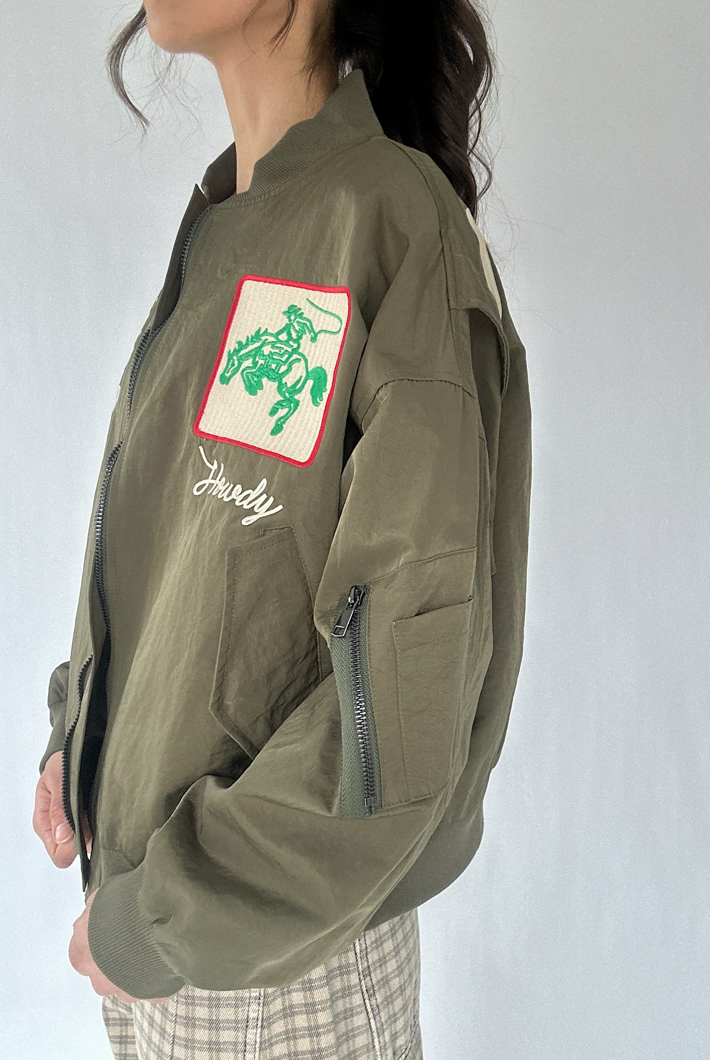 Person wearing a green jacket with a cowboy patch and cargo pocket on a white background