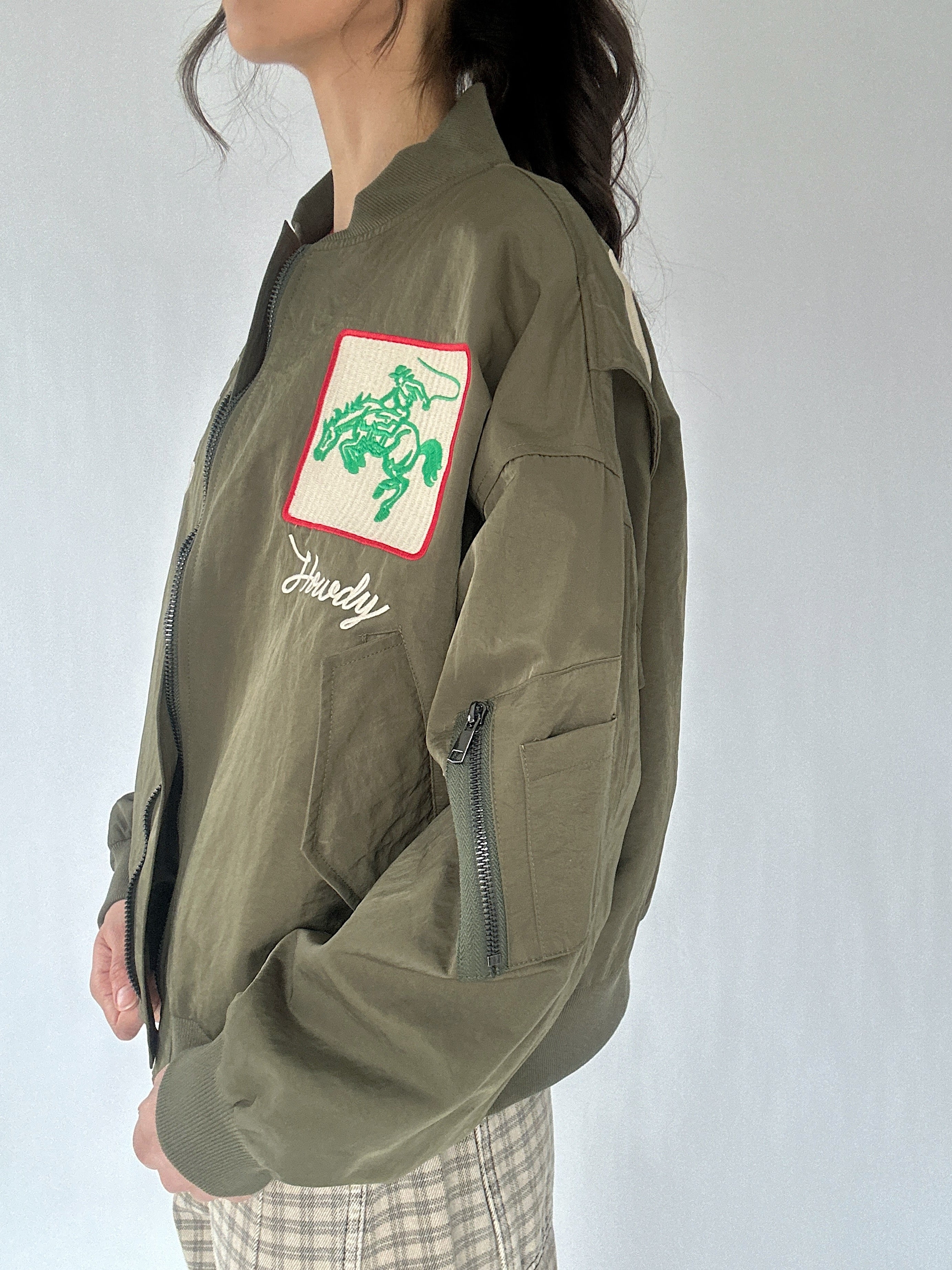 Person wearing a green jacket with a cowboy patch and cargo pocket on a white background
