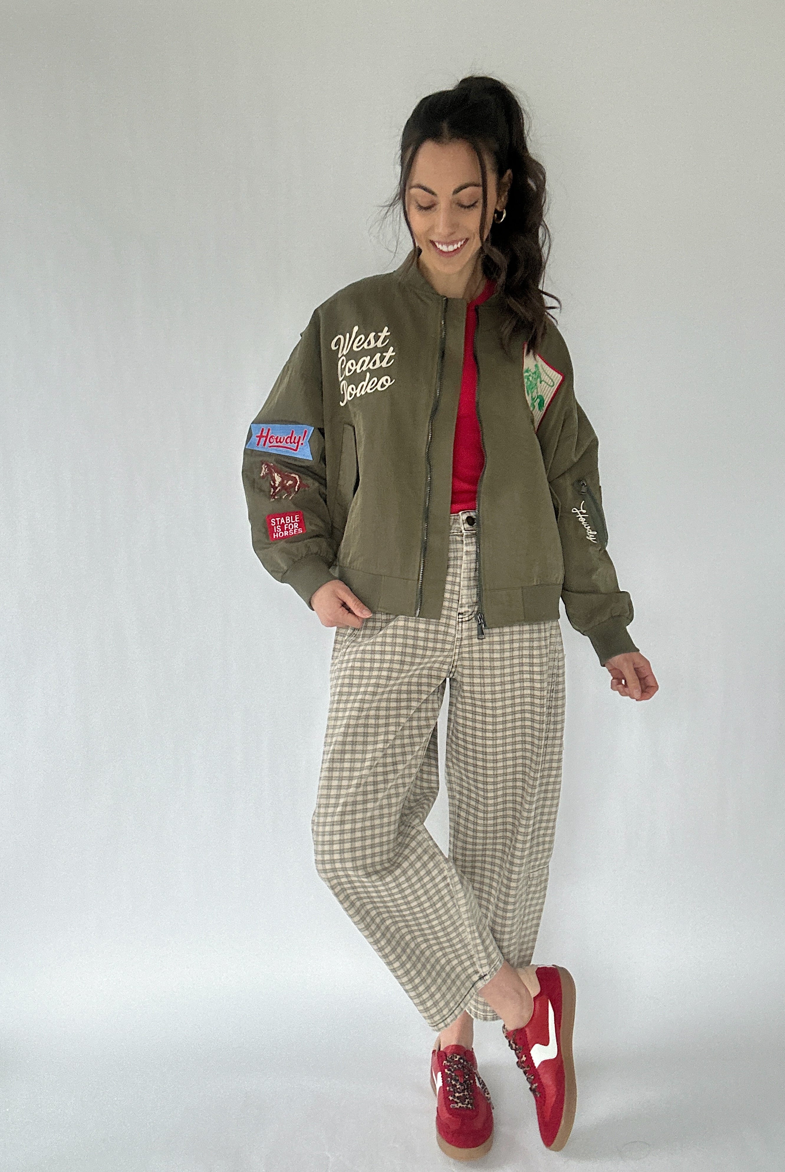 Woman wearing a green jacket with western patches, red shirt, and plaid pants on a white background