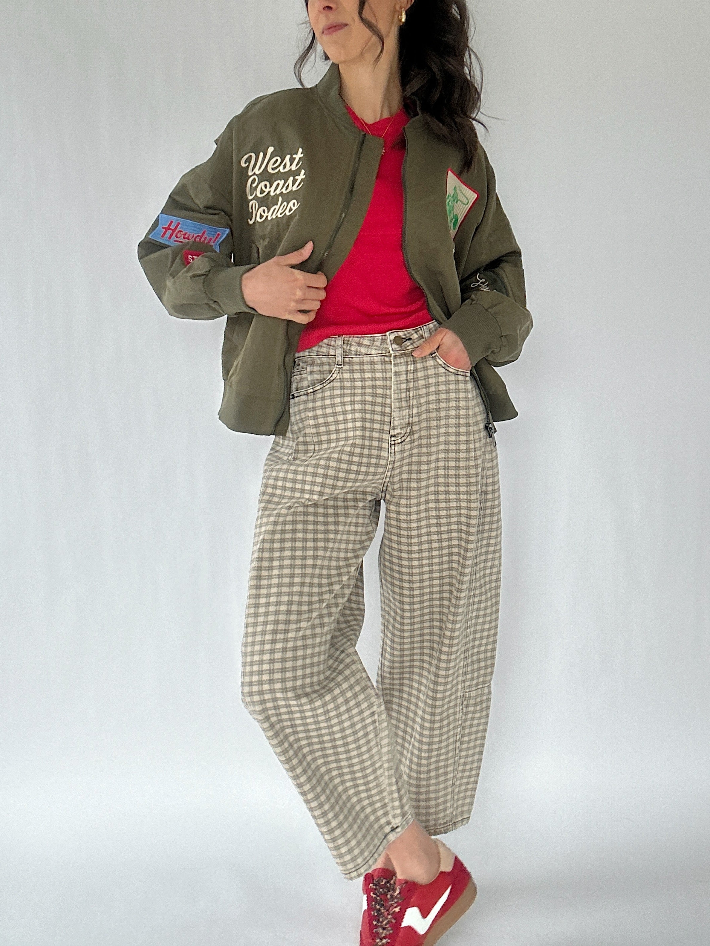 Person wearing a green jacket with text, red shirt, and checkered pants on a white background