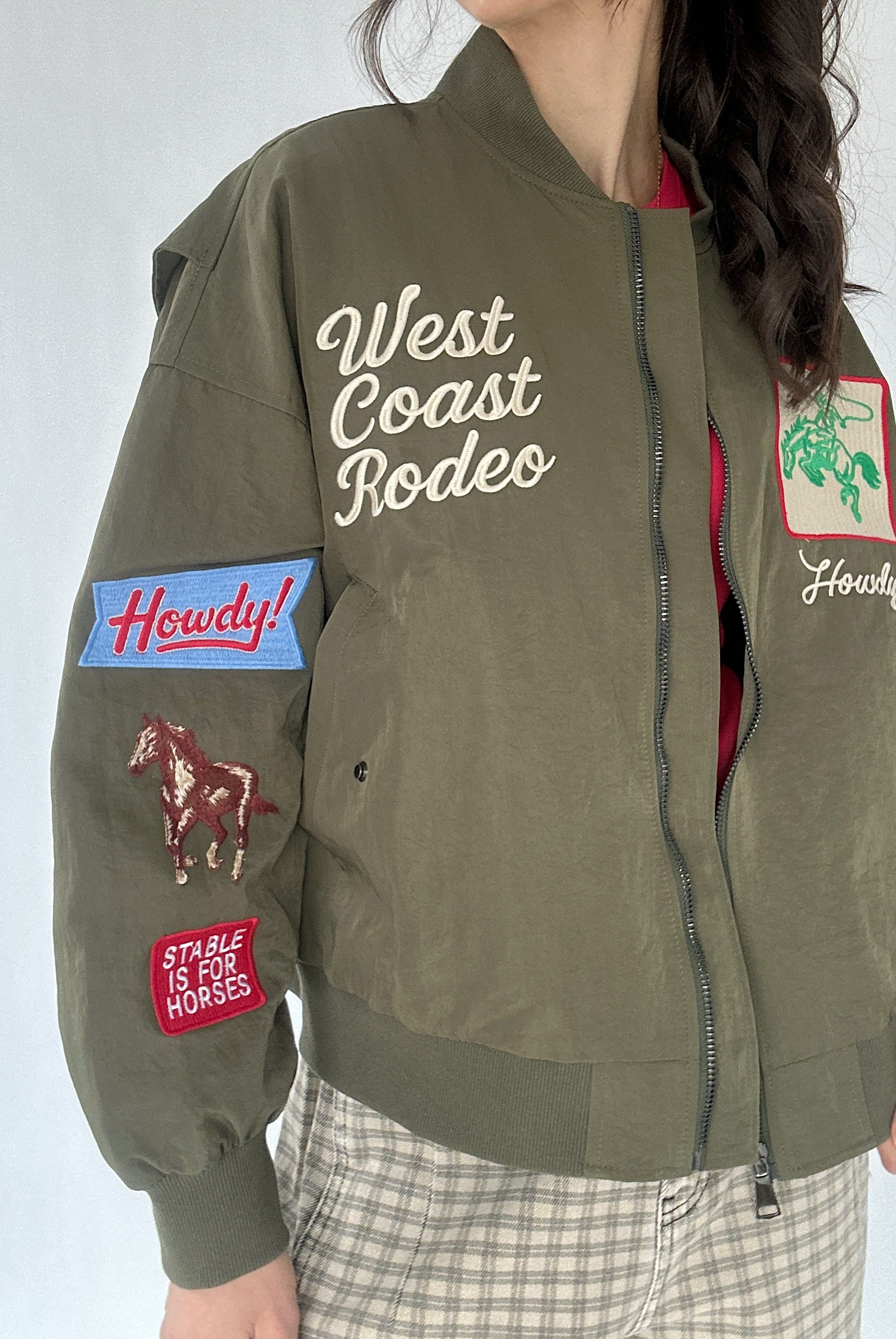 Green bomber jacket with patches and text worn by a person on a white background