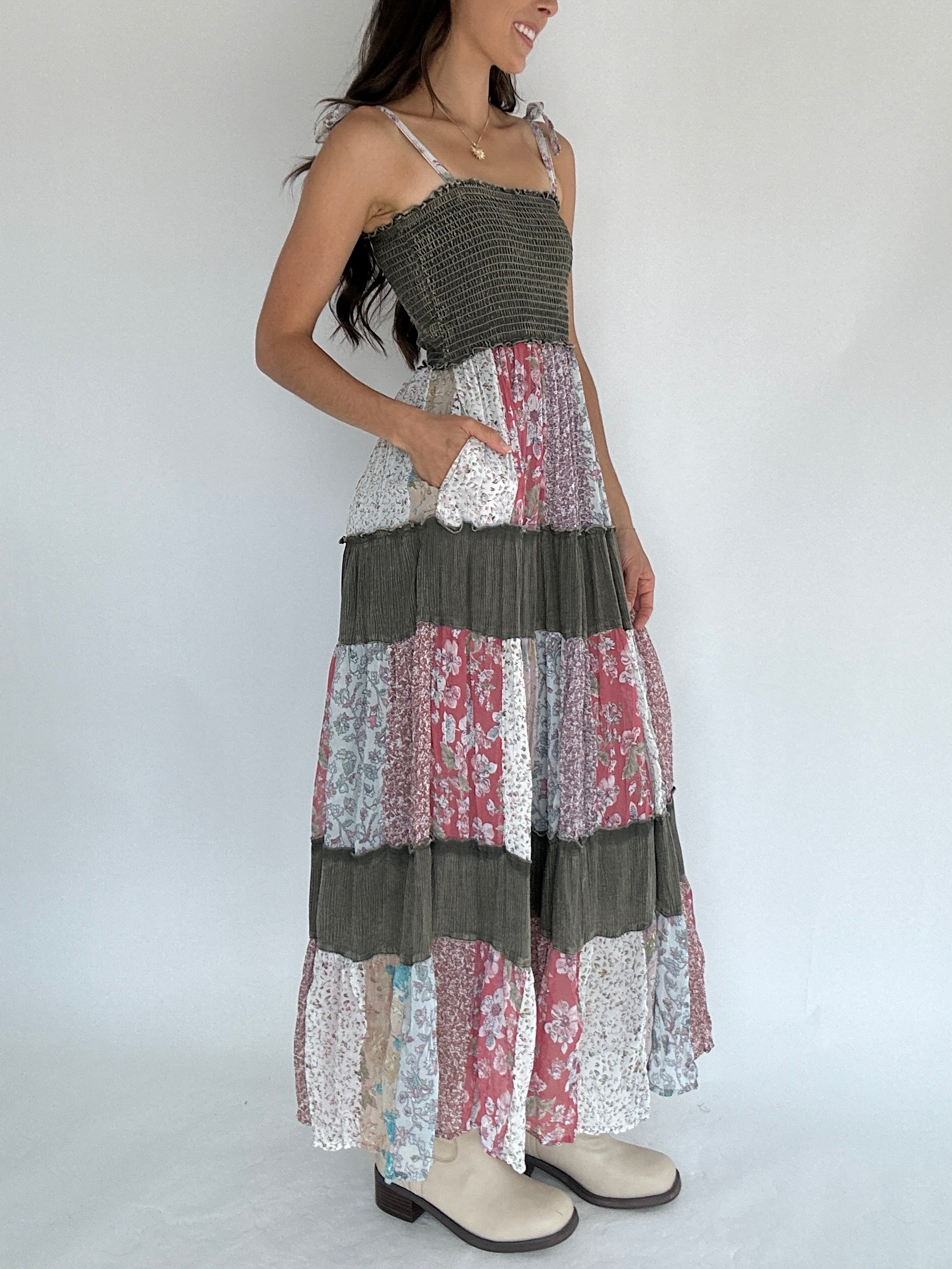 Woman wearing a patchwork dress with floral patterns on a plain background with hand in pocket side view