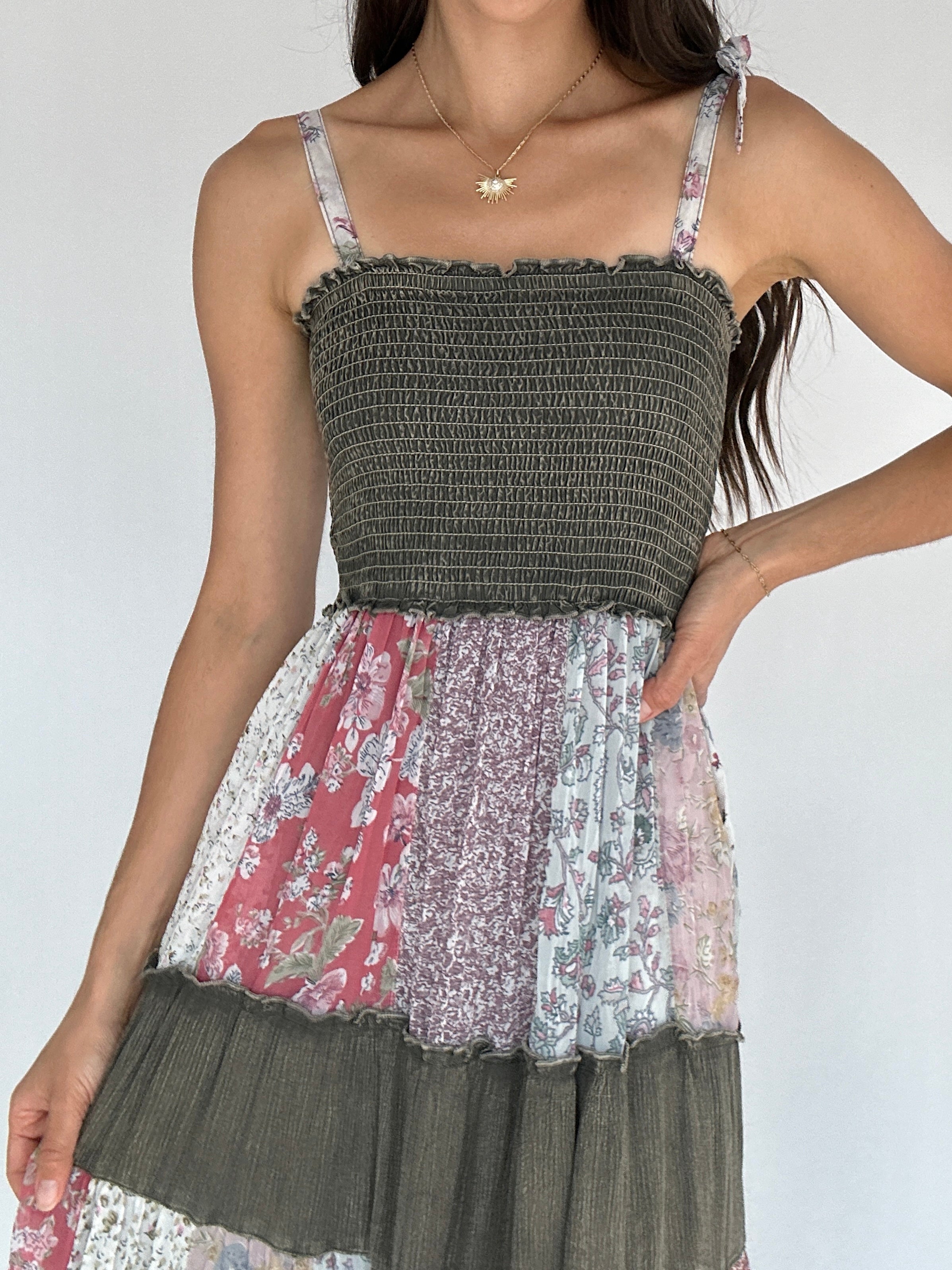 Woman wearing a patchwork dress with floral and solid patterns on a plain background showing smocked square neckline and tie straps