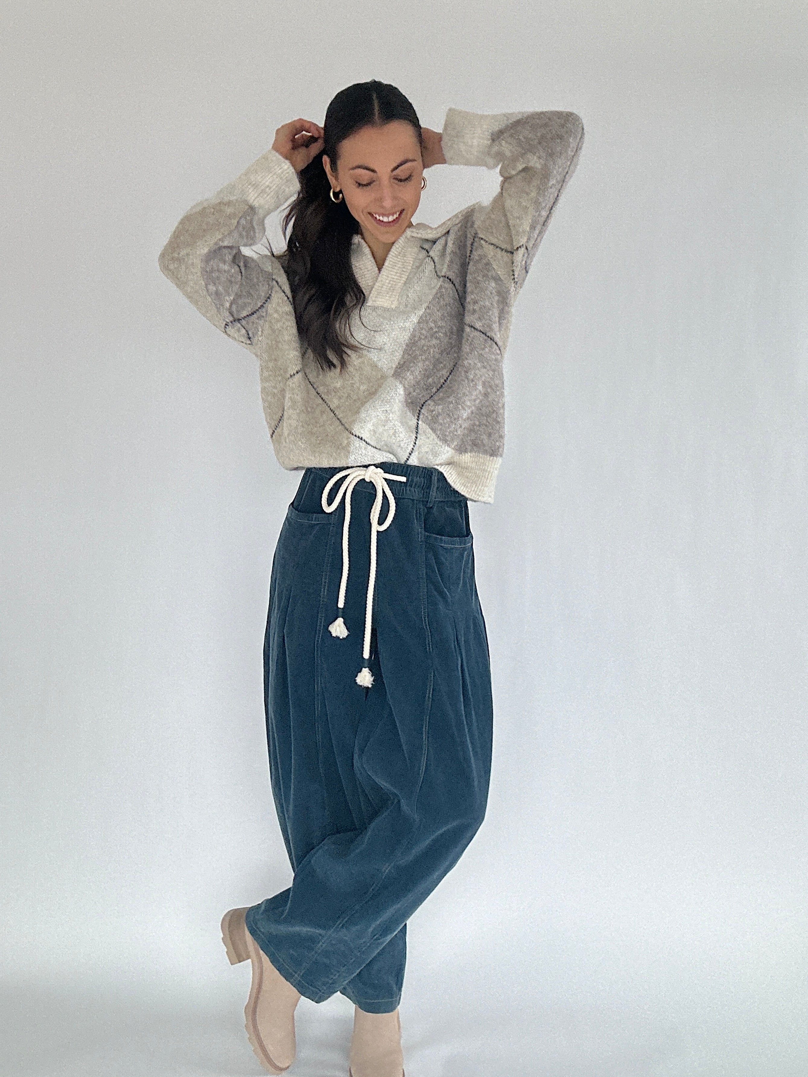Woman wearing an argyle patterned sweater and blue pants on a white background