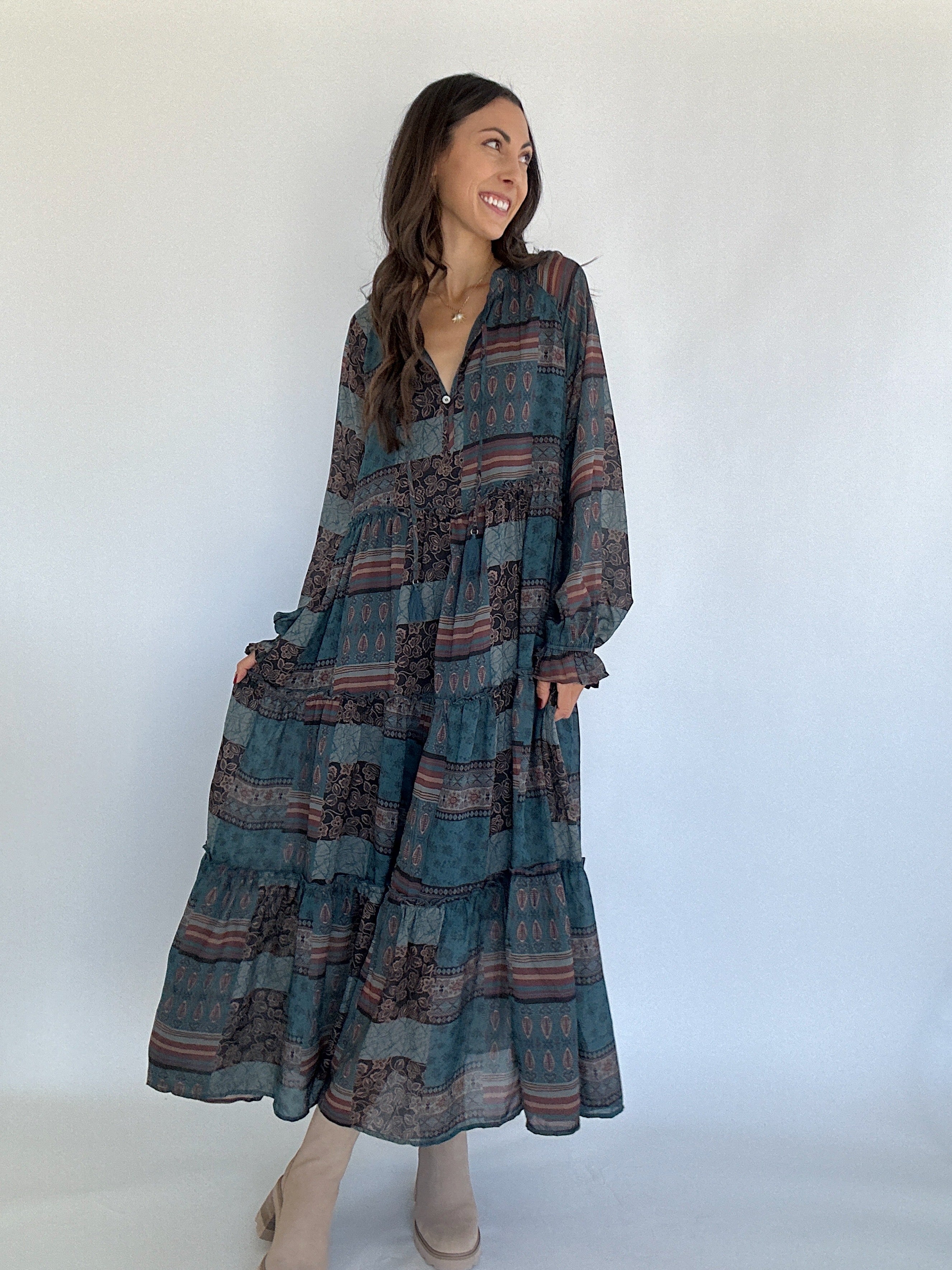 Woman wearing a pine green long, patterned dress against a white background