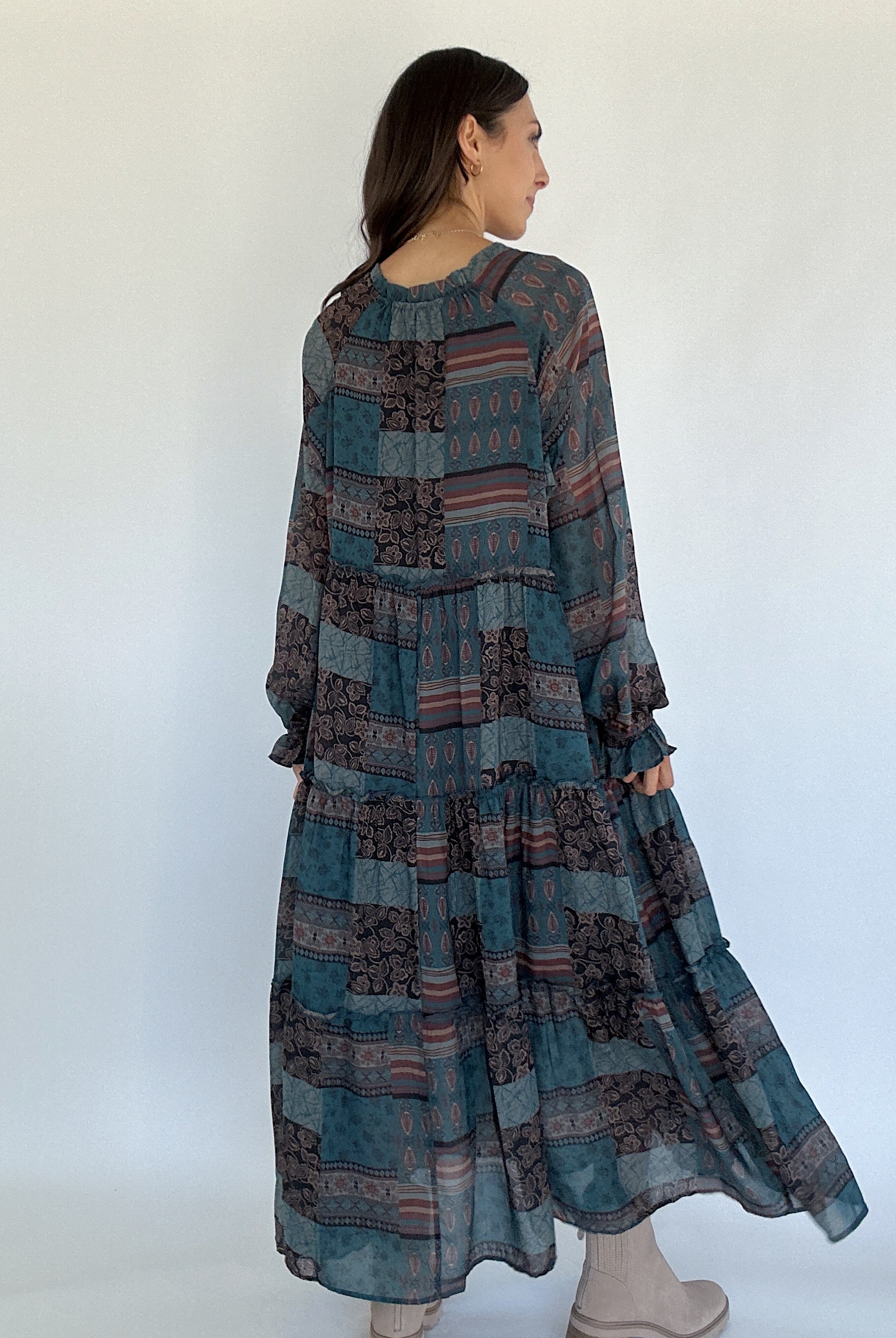 Woman wearing a long, patterned dress against a white background showing back
