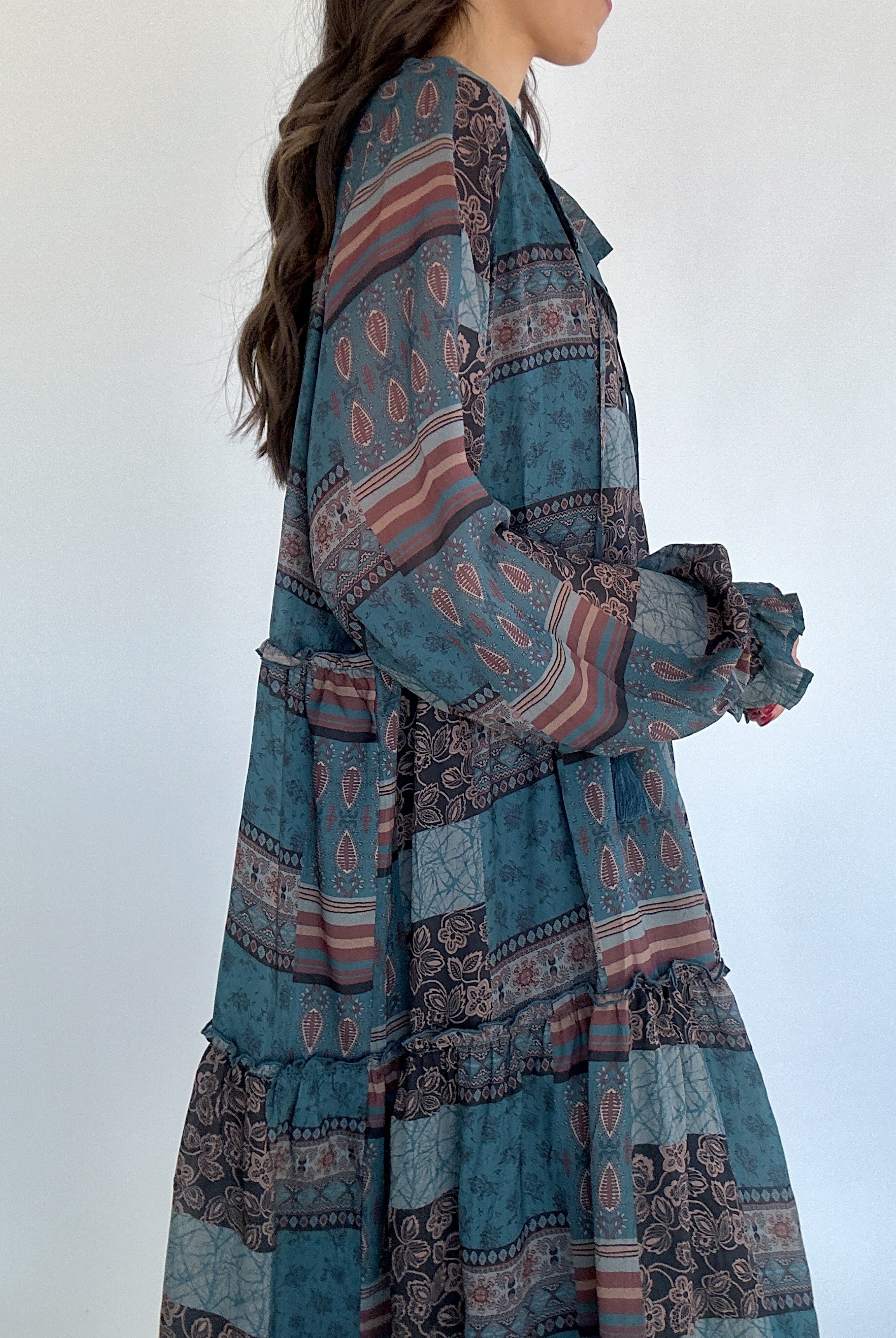 Long, patterned dress with a mix of blue and brown colors on a white background showing sleeve and side