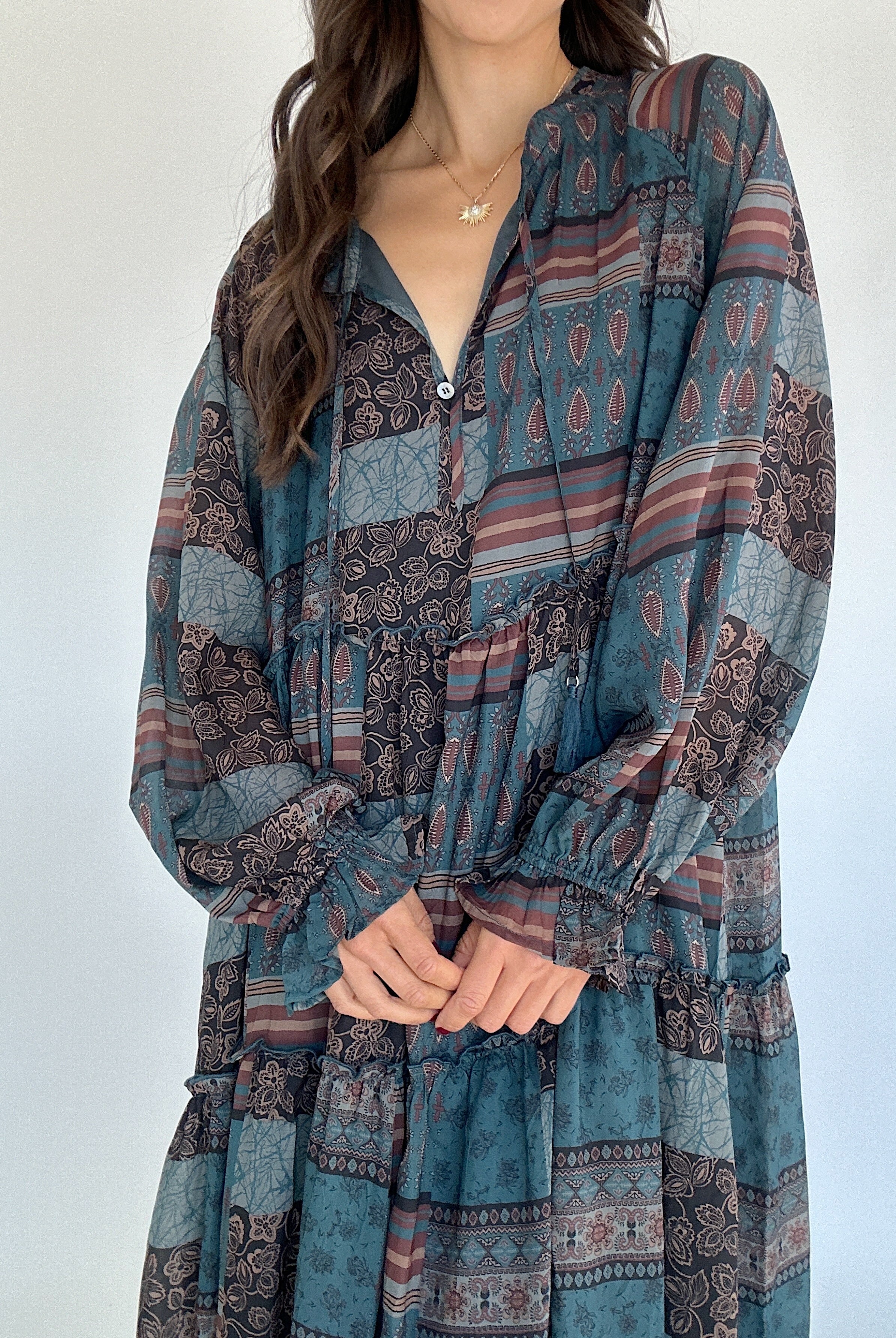 Woman wearing a long-sleeve, patterned dress against a white background showing neckline