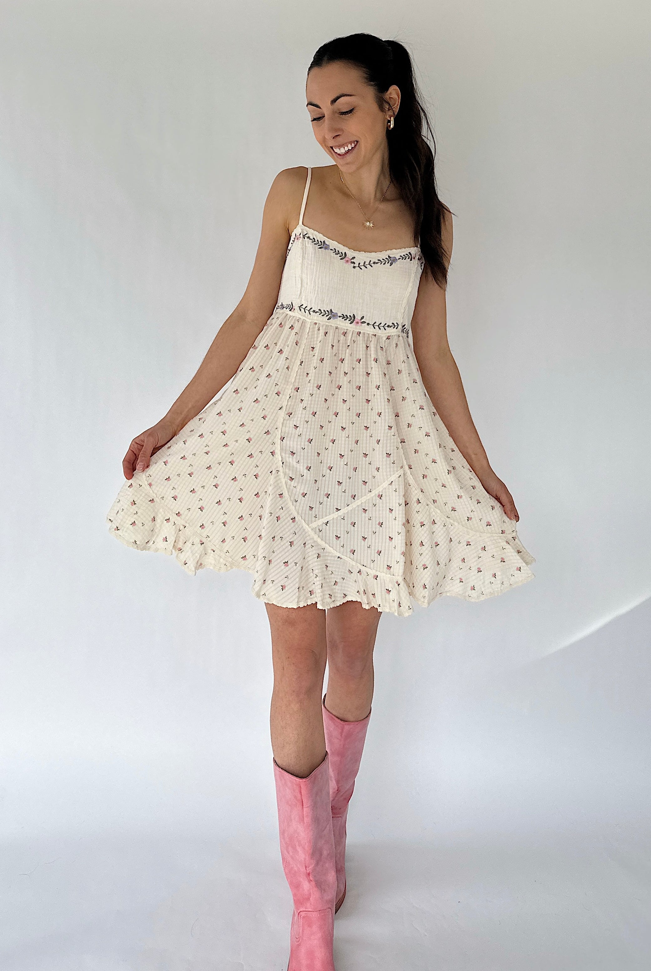 Woman wearing a white dress with floral patterns and pink knee-high boots on a plain background