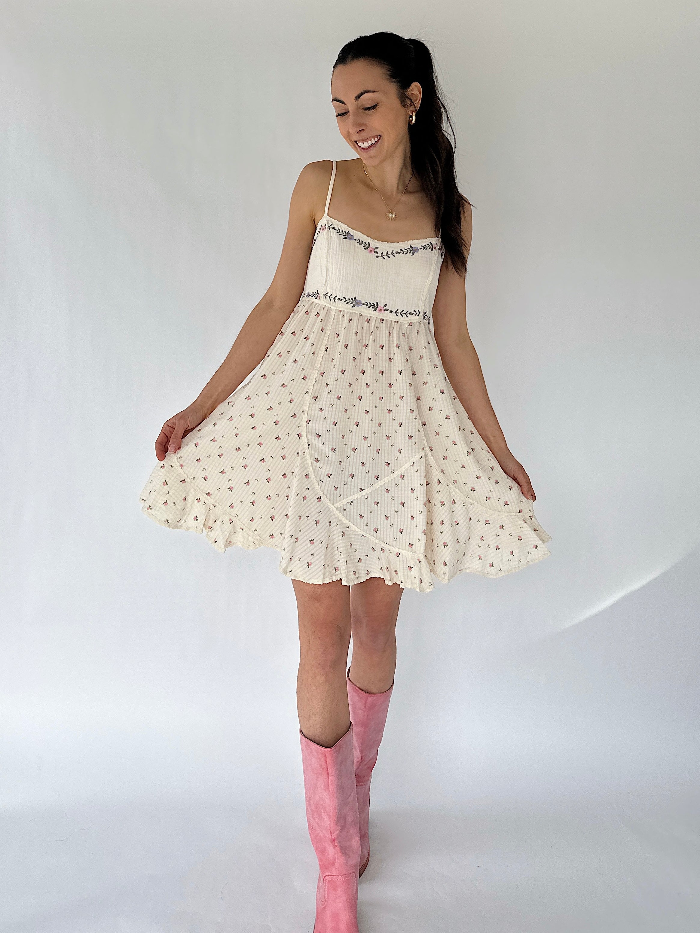 Woman wearing a white dress with floral patterns and pink knee-high boots on a plain background