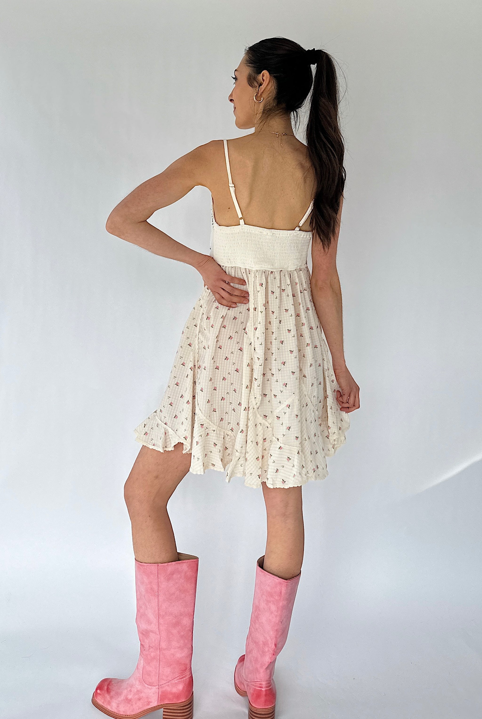 Woman wearing a white floral mini dress with pink boots on a plain background
