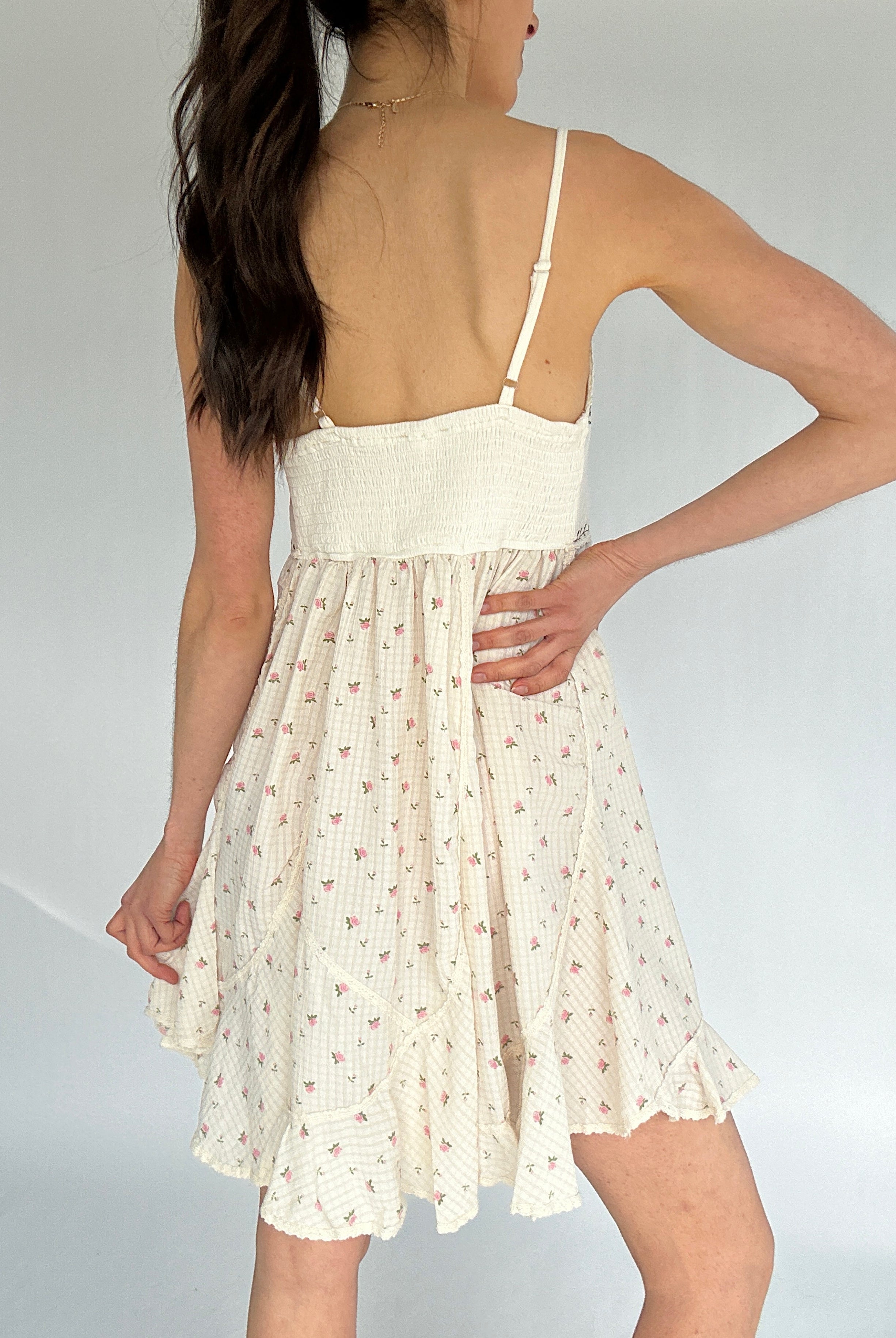 Woman wearing a white floral dress against a plain background showing smocked back