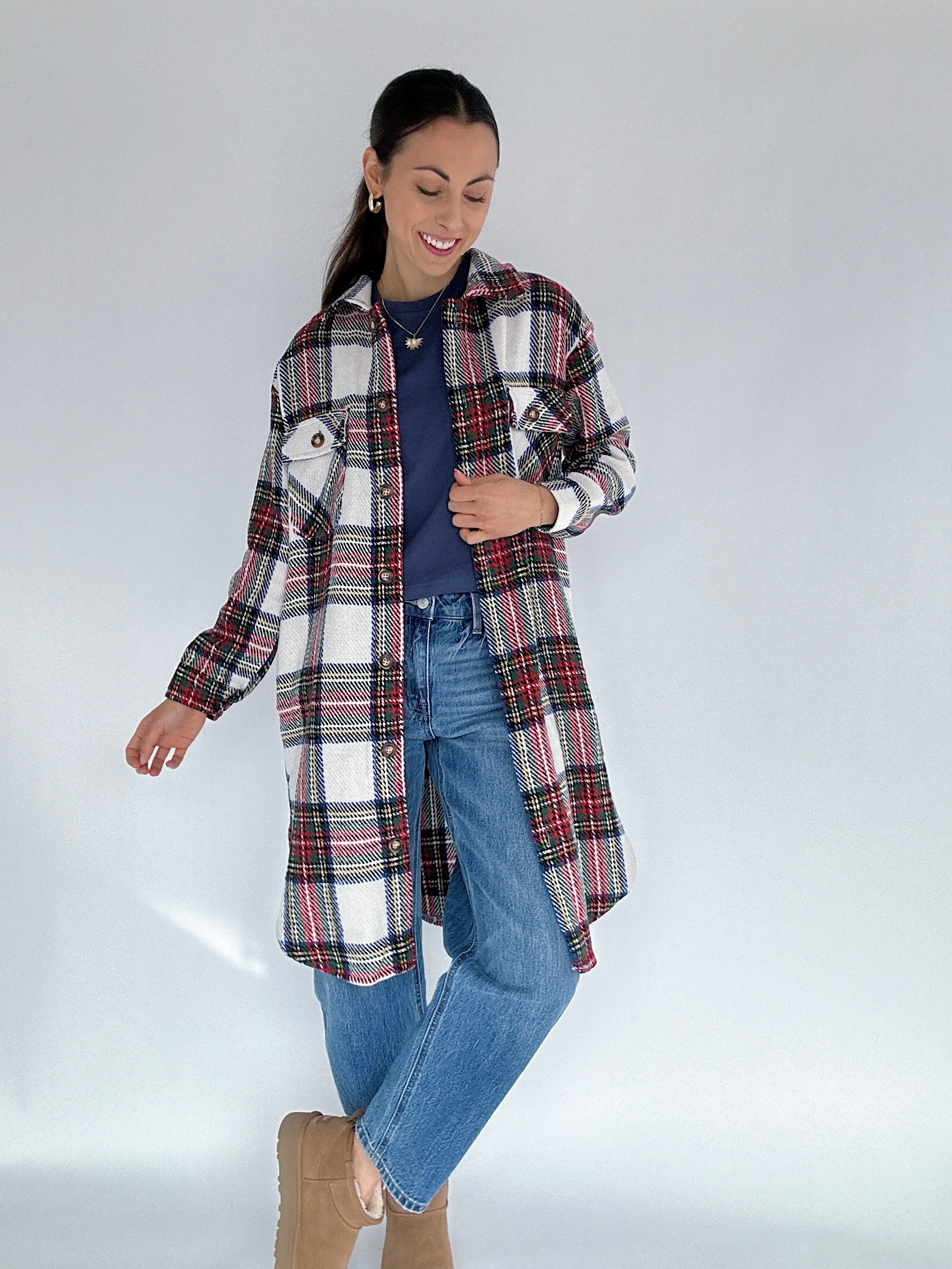 Woman wearing a long plaid jacket over a blue top and jeans on a white background