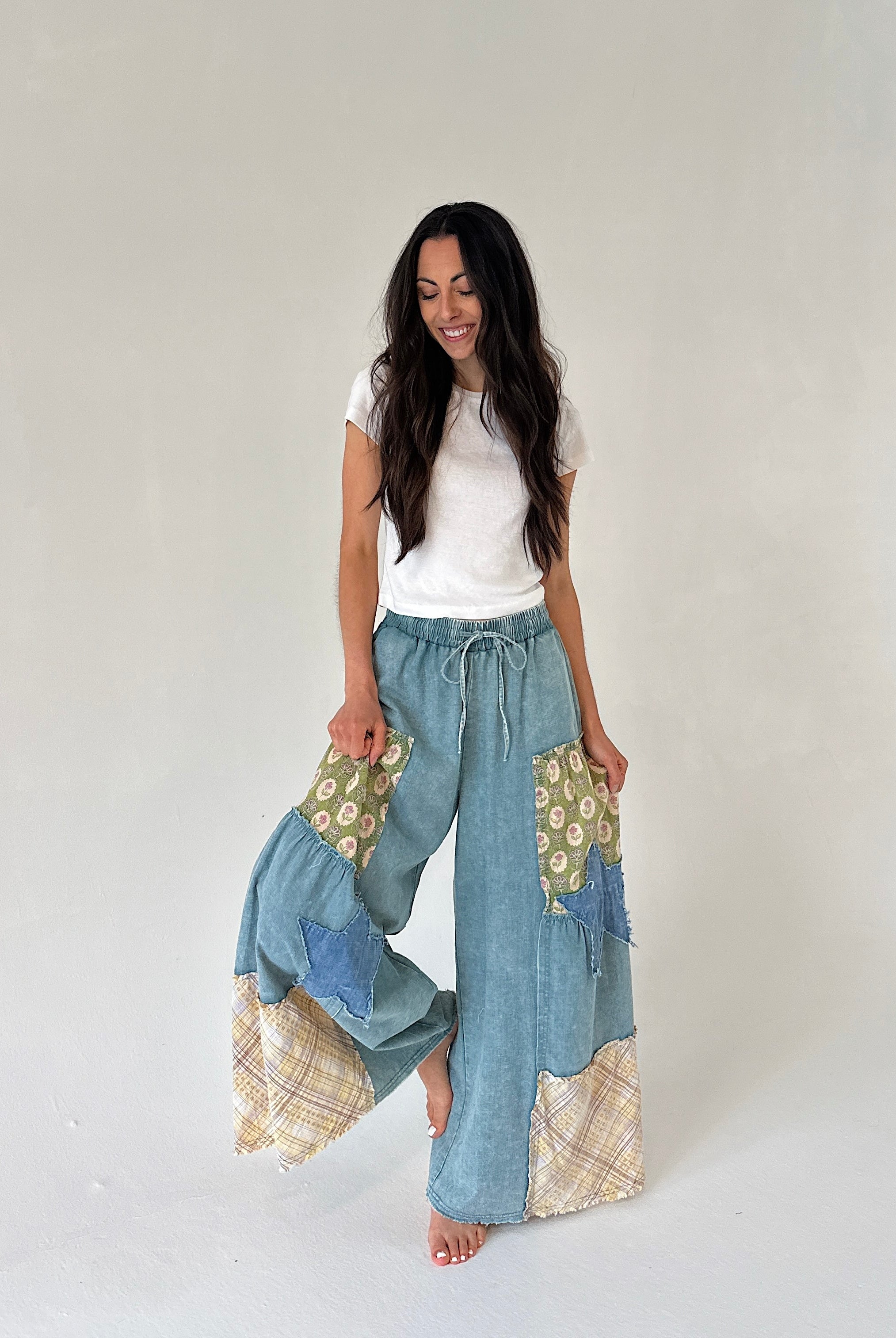 Woman wearing a white top and patchwork pants on a plain background