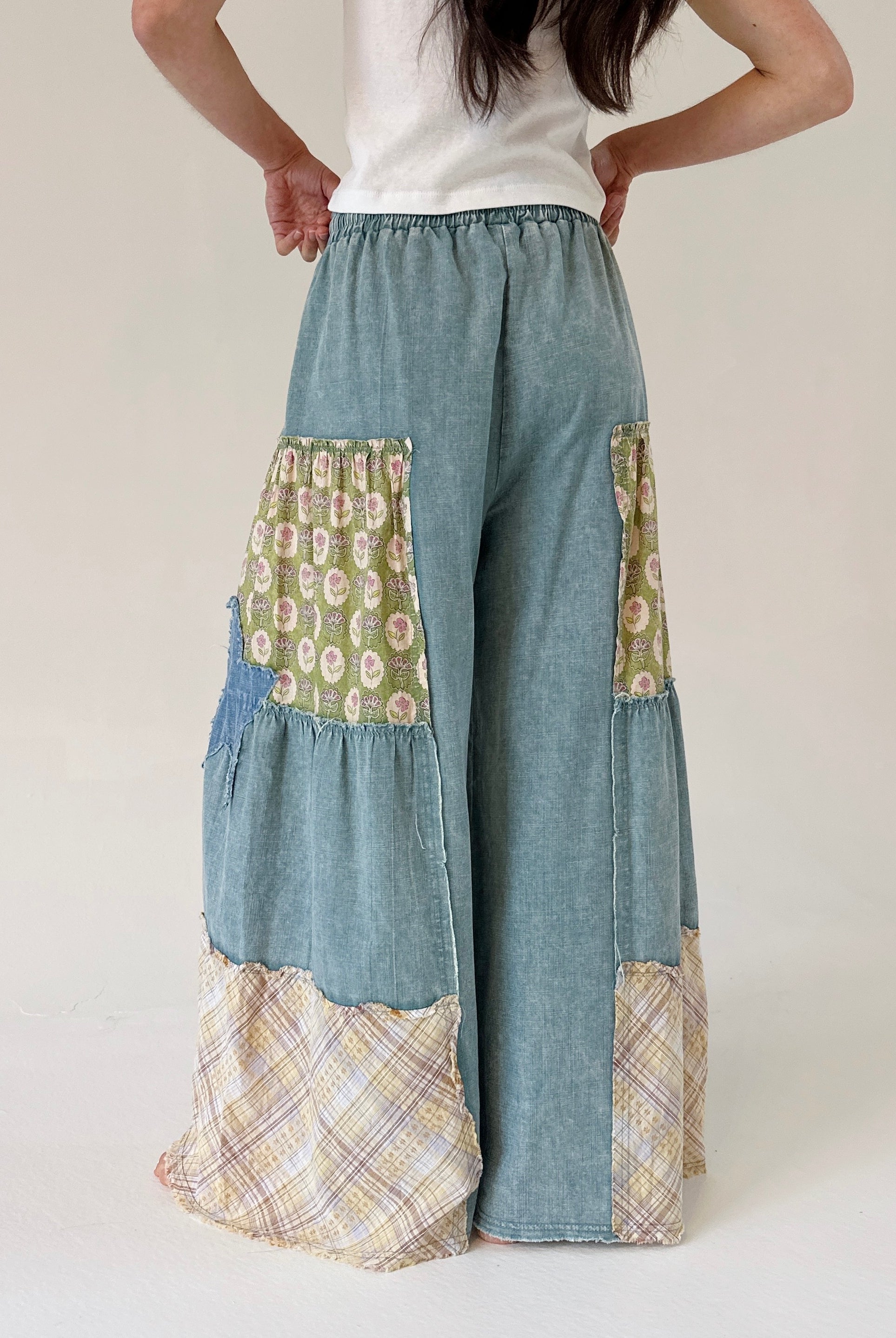 Patchwork pants with floral and plaid patterns worn by a person on a white background from back