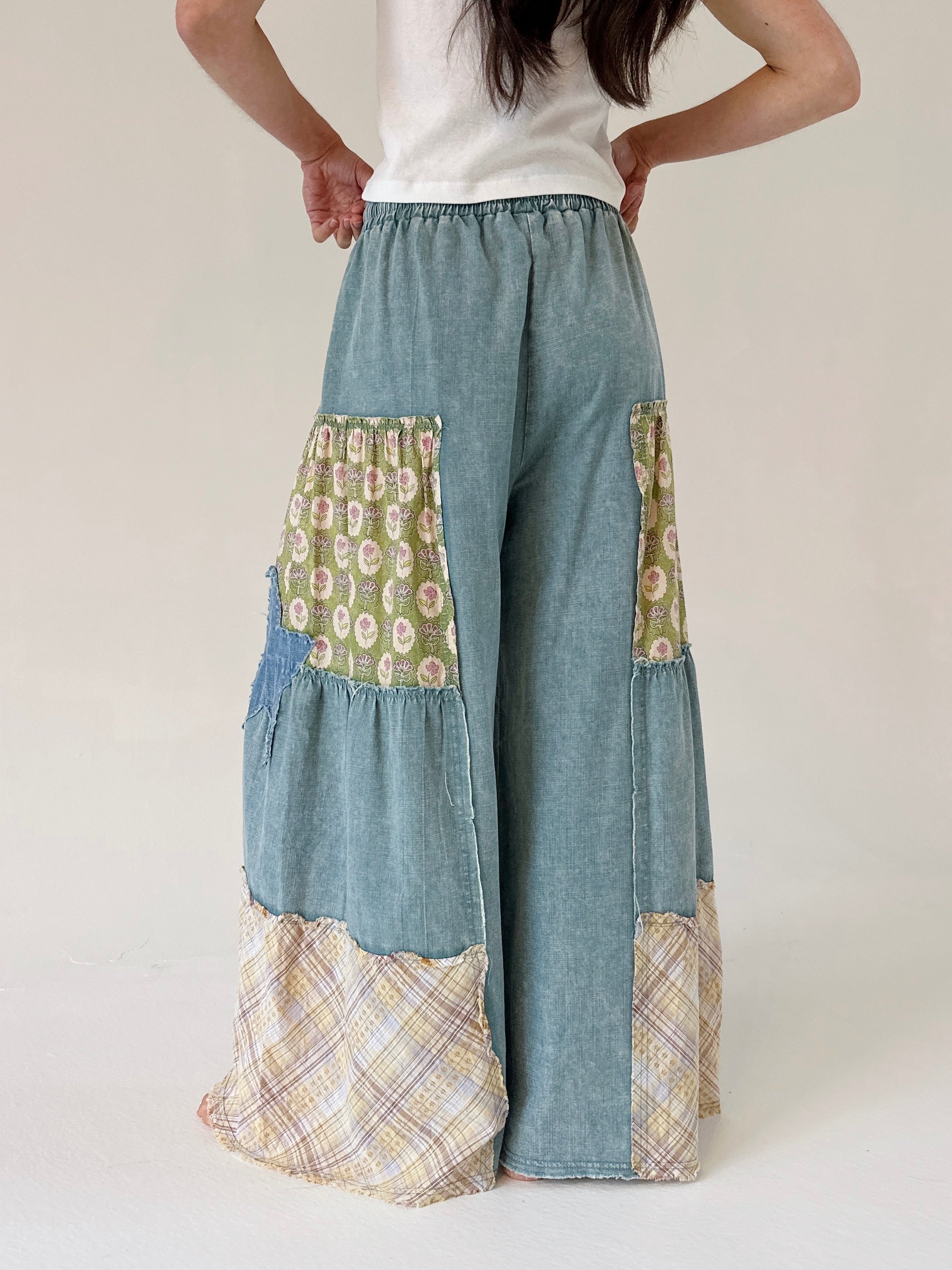 Patchwork pants with floral and plaid patterns worn by a person on a white background from back