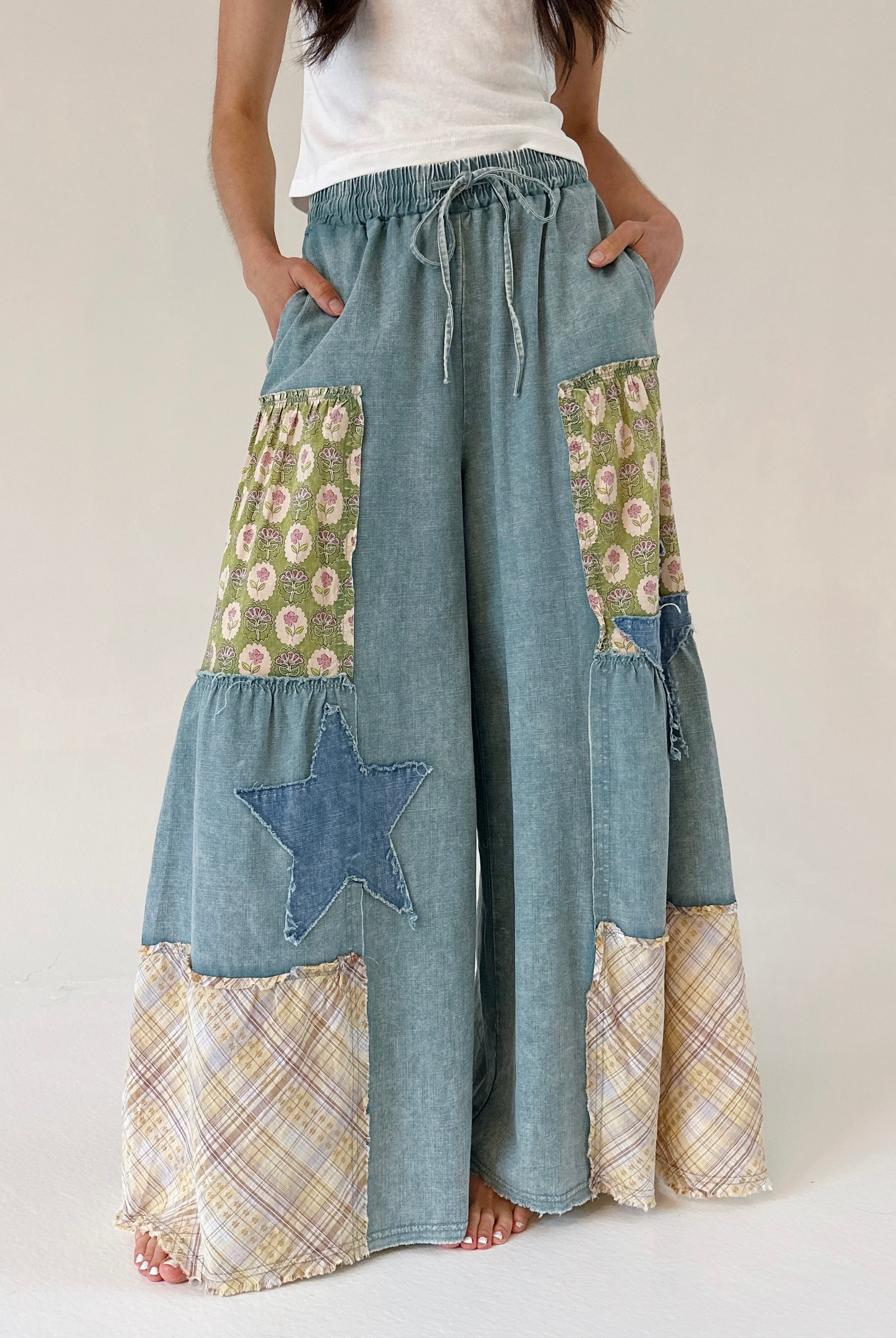 Person wearing a patchwork denim wide leg pants with floral and star and plaid patches on a plain background