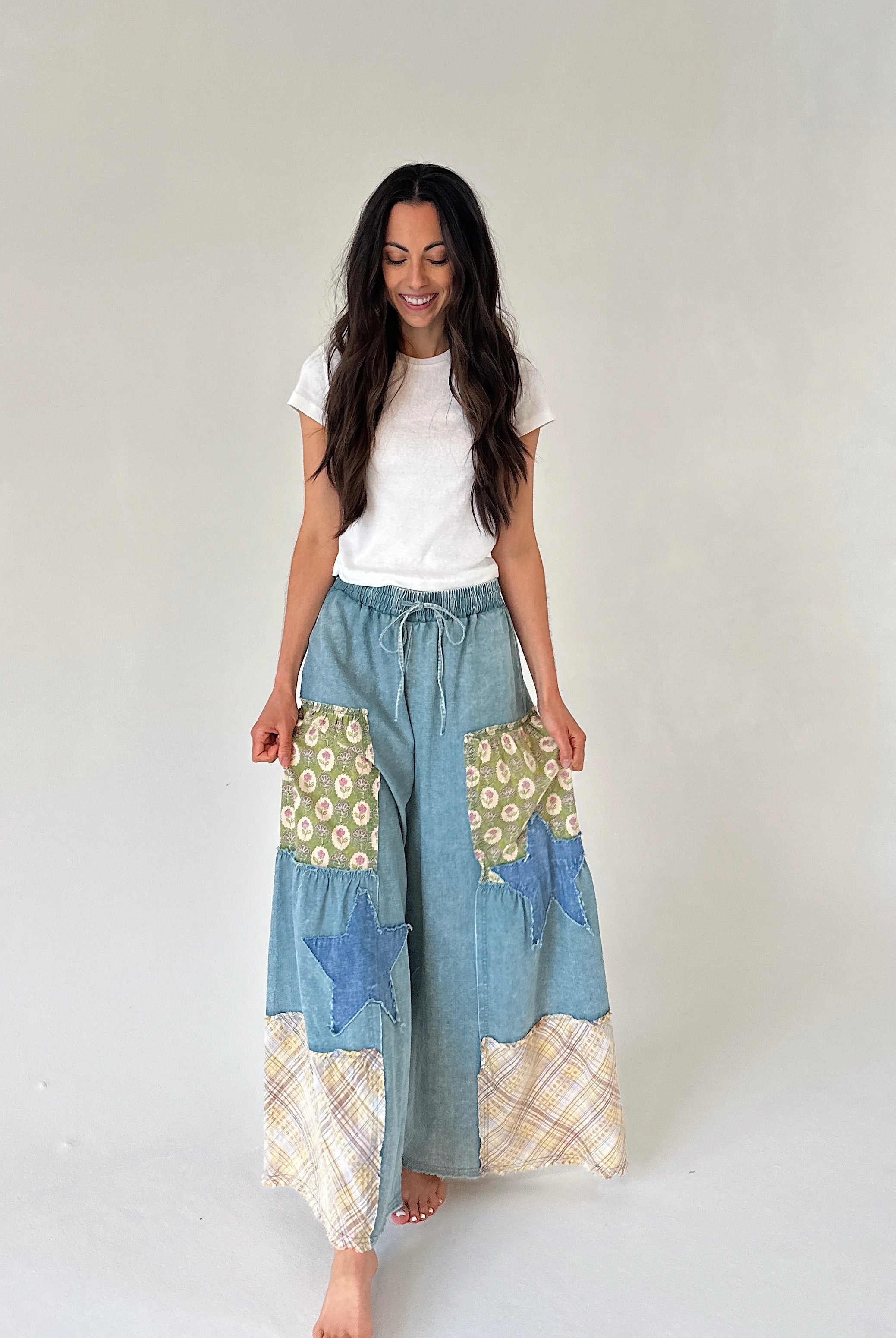 Woman wearing a white t-shirt and patchwork denim wide leg pants on a plain background