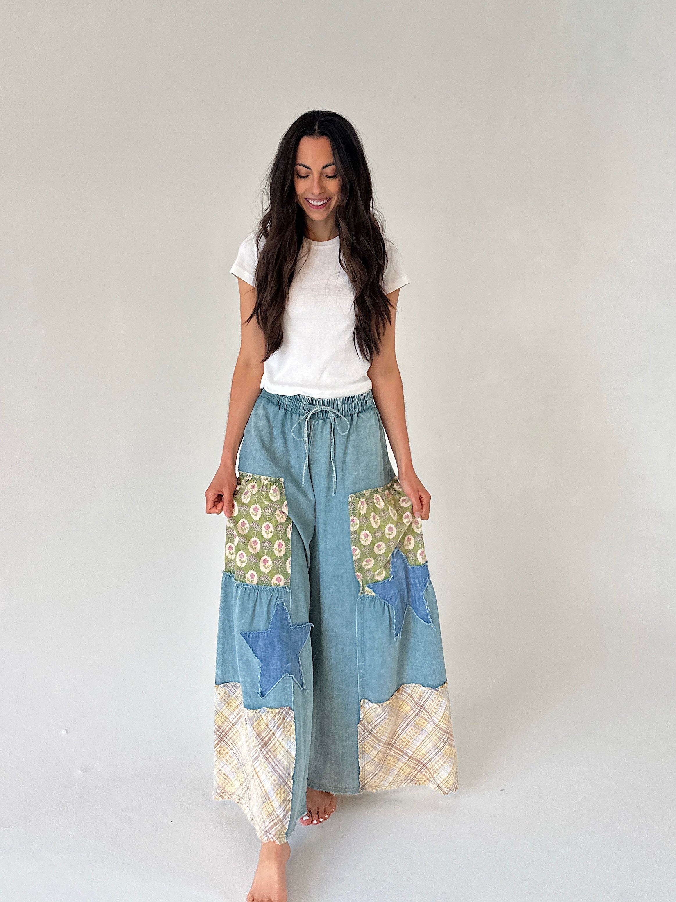 Woman wearing a white t-shirt and patchwork denim wide leg pants on a plain background