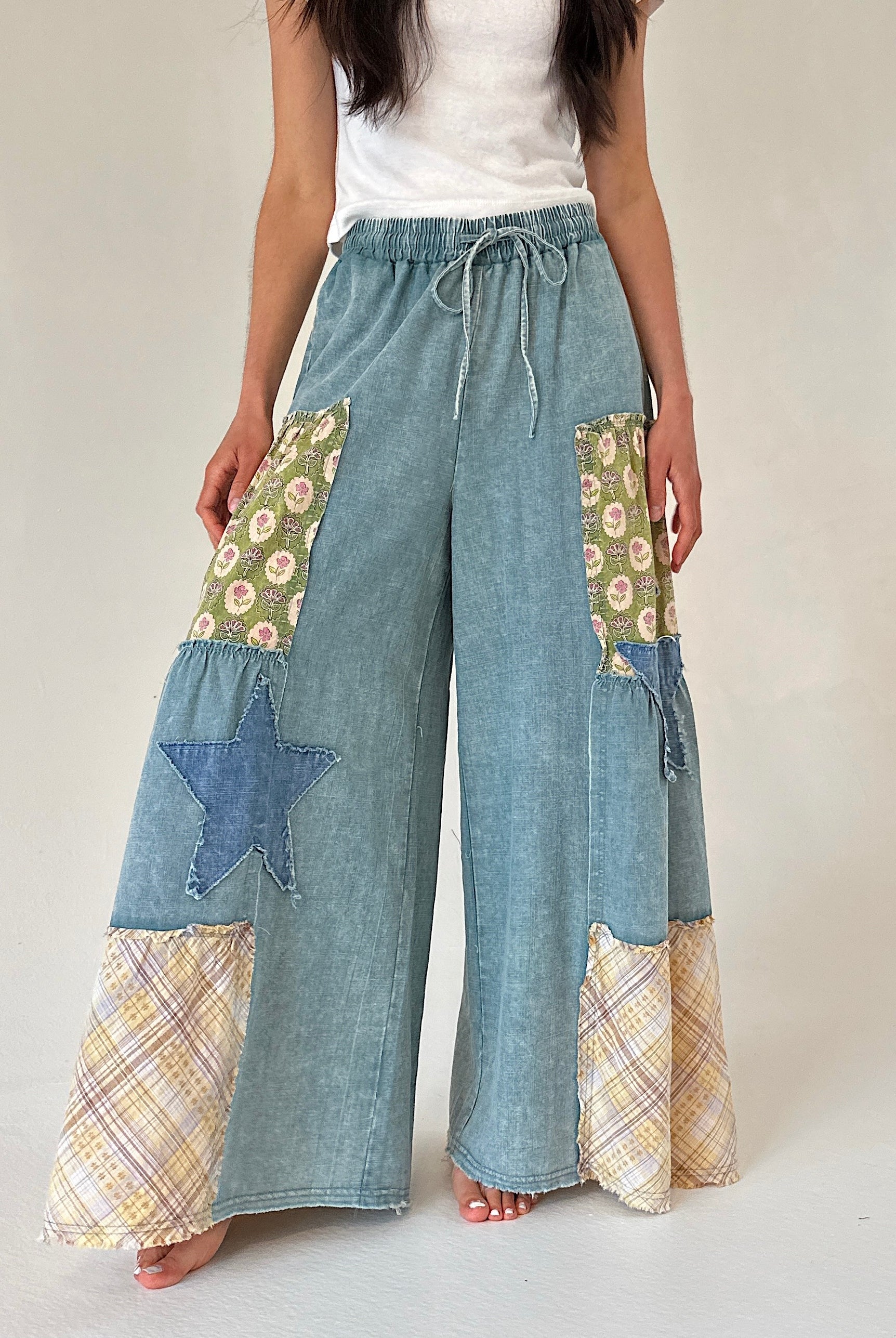 Person wearing patchwork denim pants with floral and star patterns on a plain background