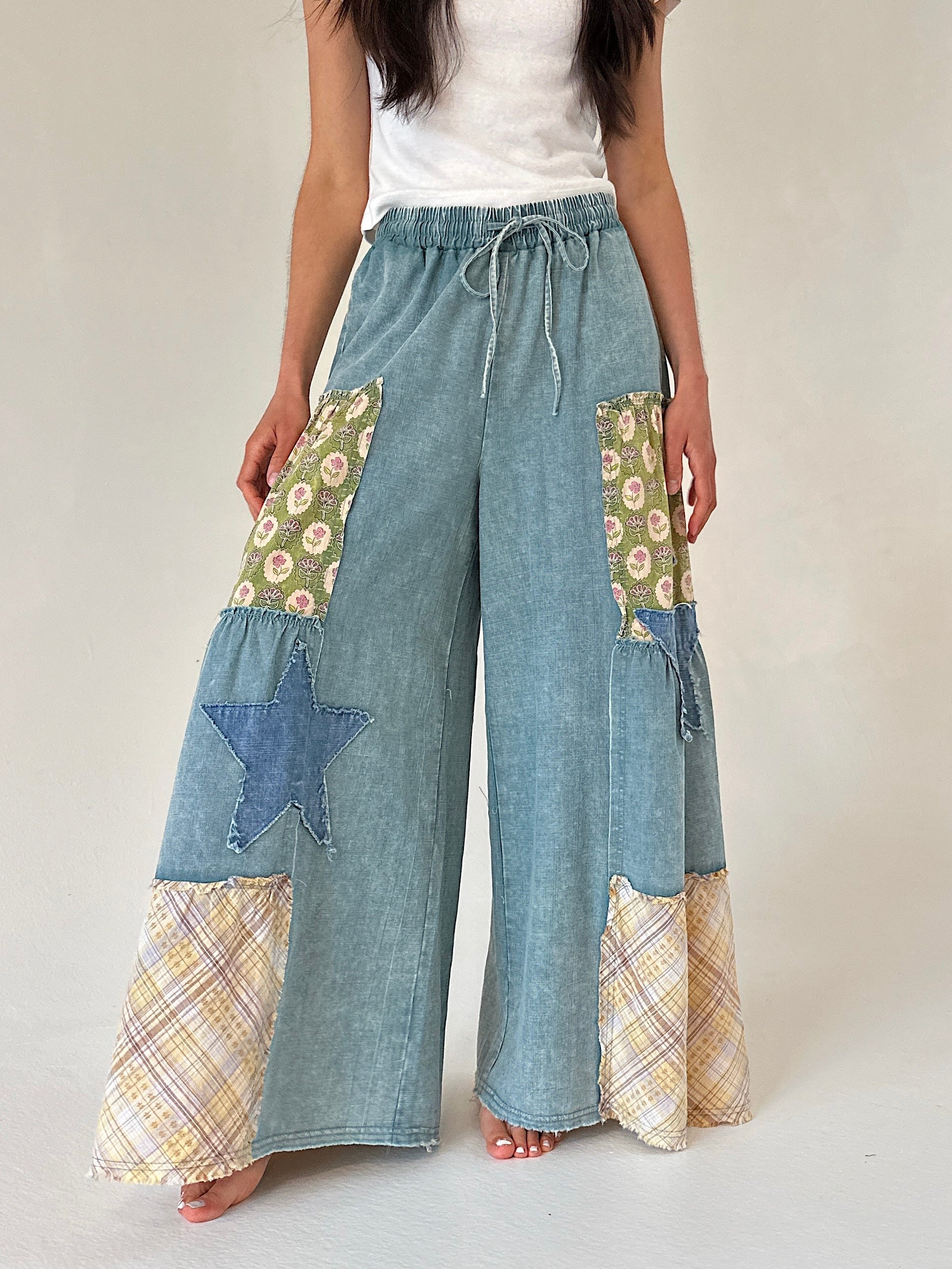 Person wearing patchwork denim pants with floral and star patterns on a plain background