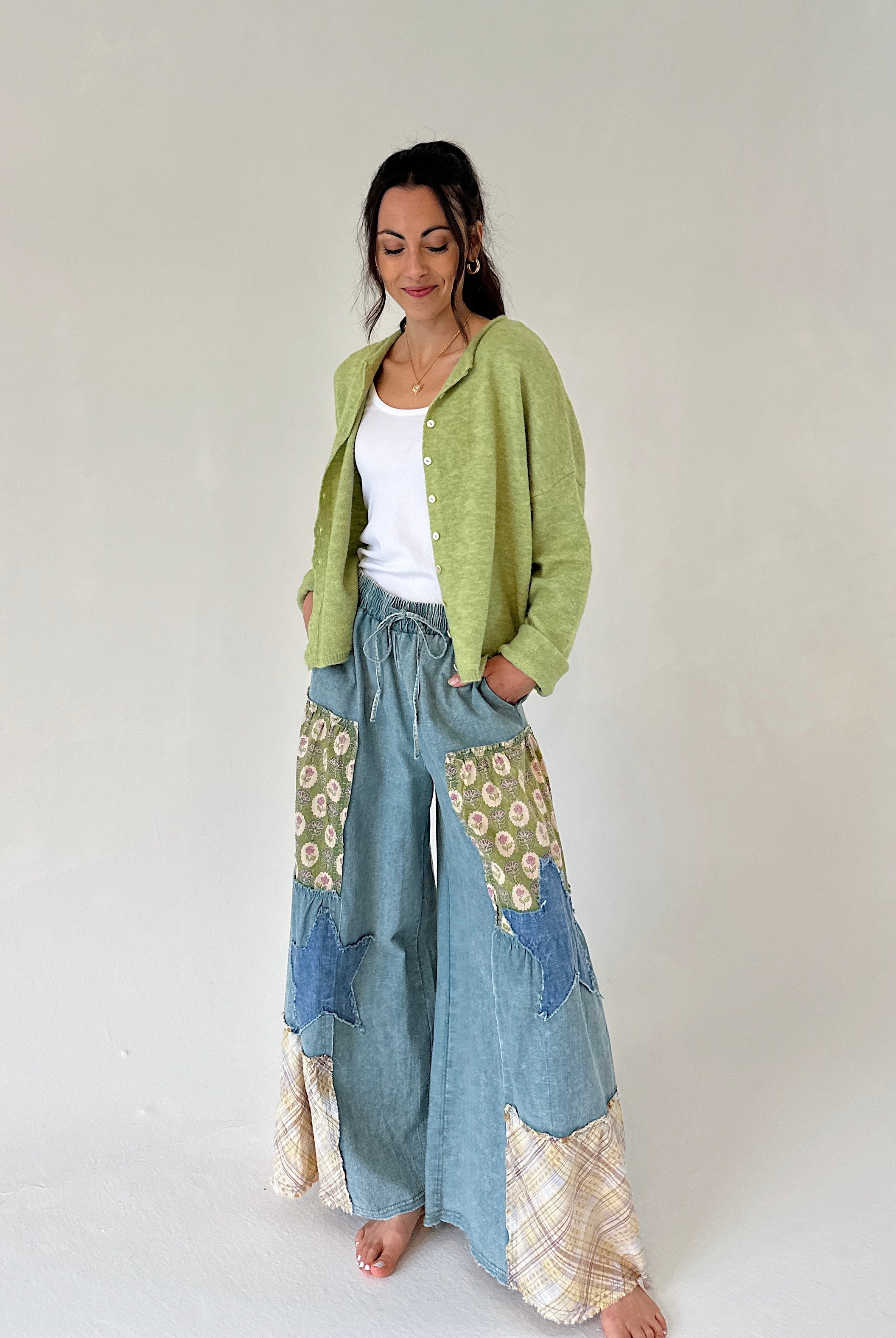Woman wearing a green cardigan and patterned denim pants on a white background