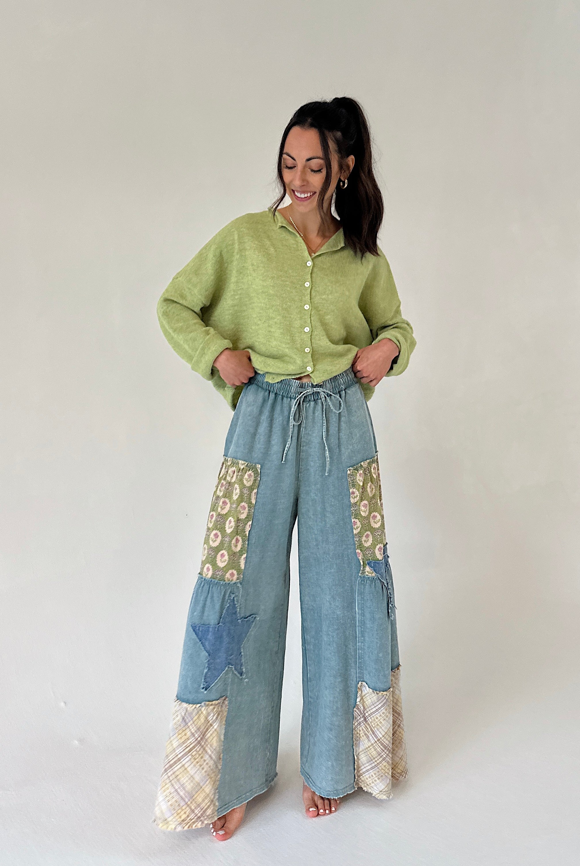 Woman wearing a green cardigan and blue patchwork pants on a white background
