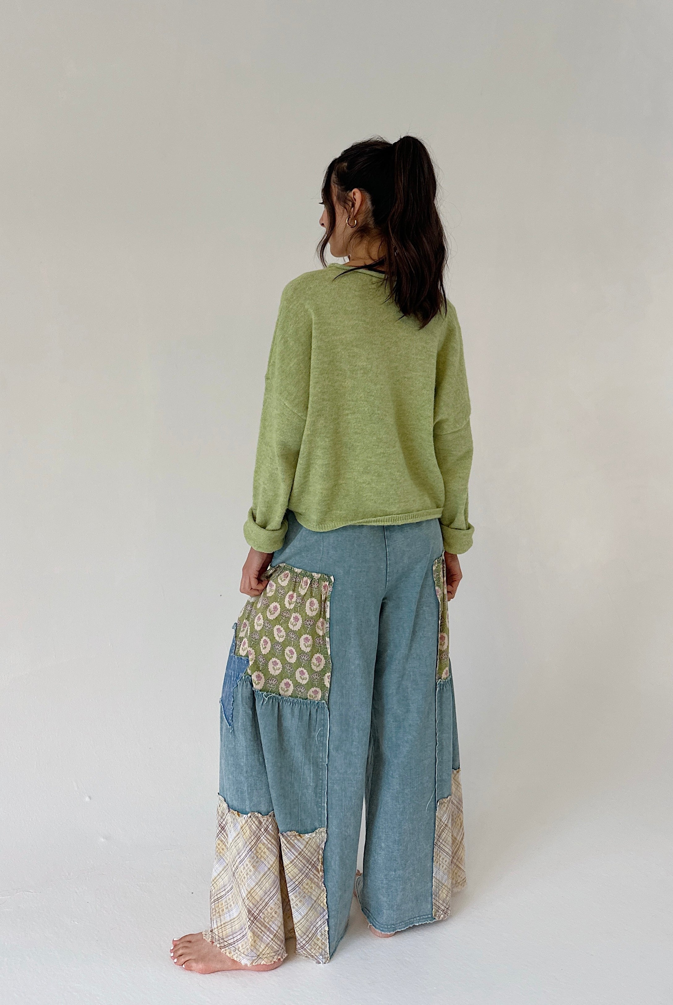 Person wearing a green sweater and blue patchwork pants on a white background