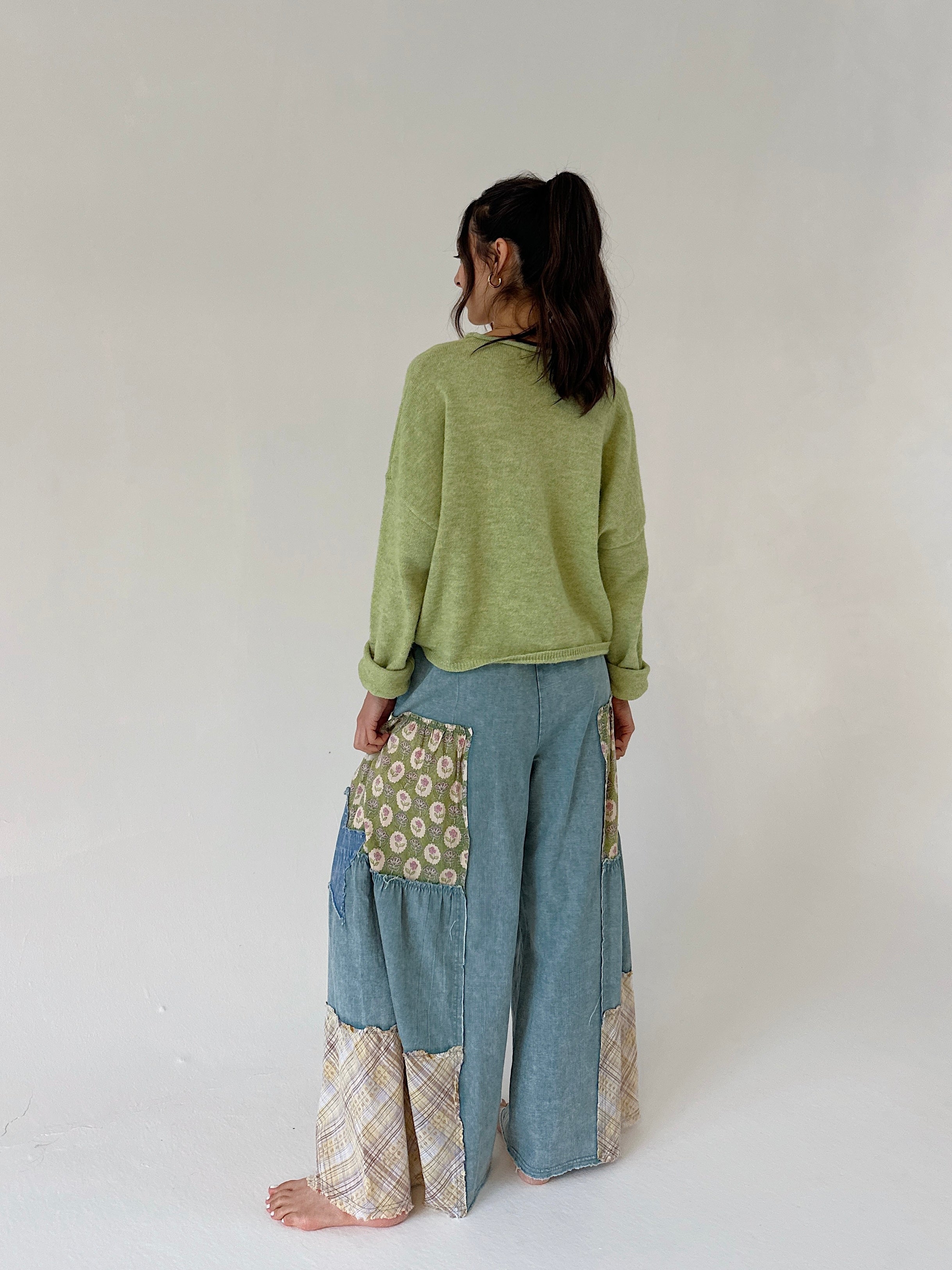 Person wearing a green sweater and blue patchwork pants on a white background