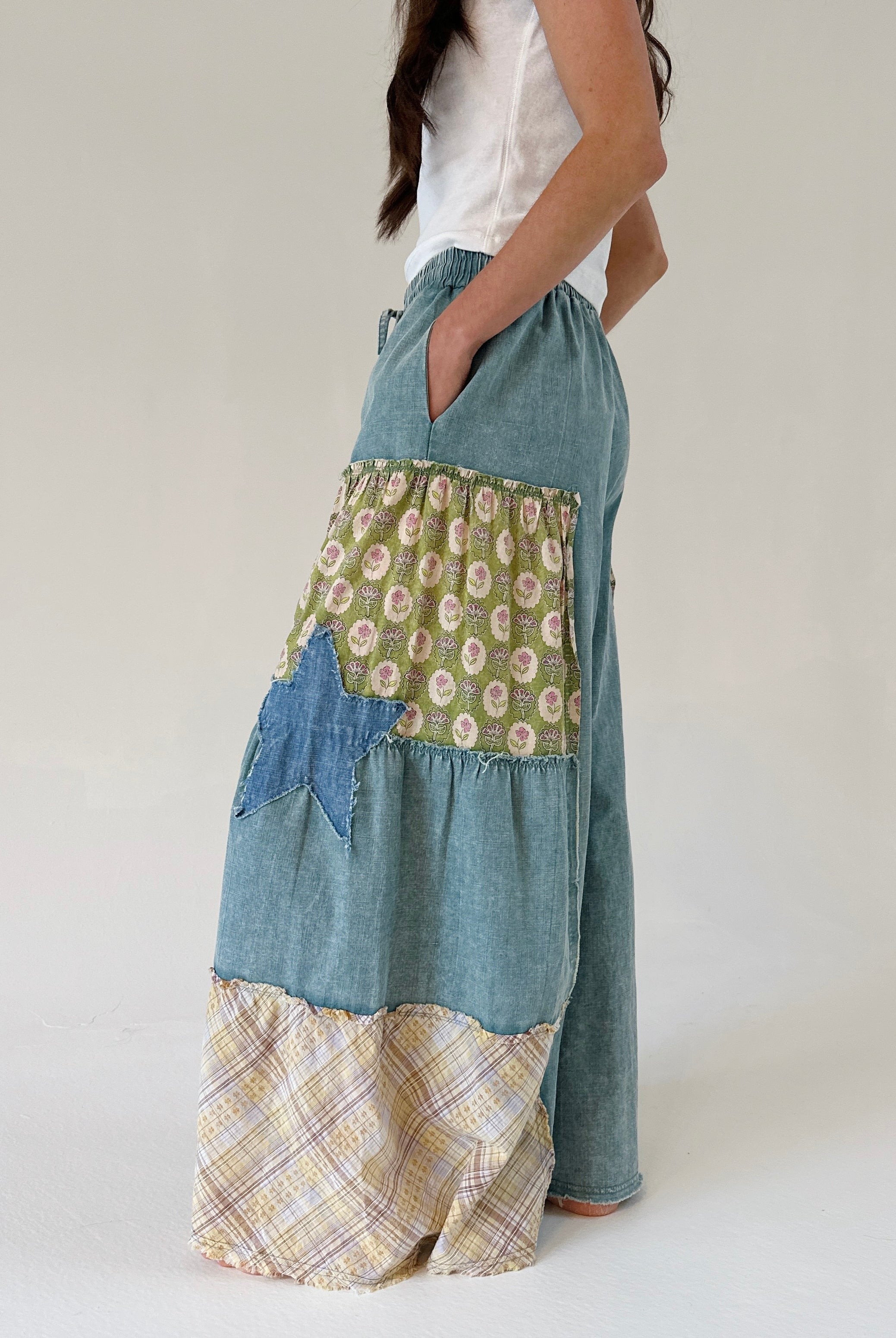 Person wearing patchwork pants with floral, plaid, and denim patterns on a white background