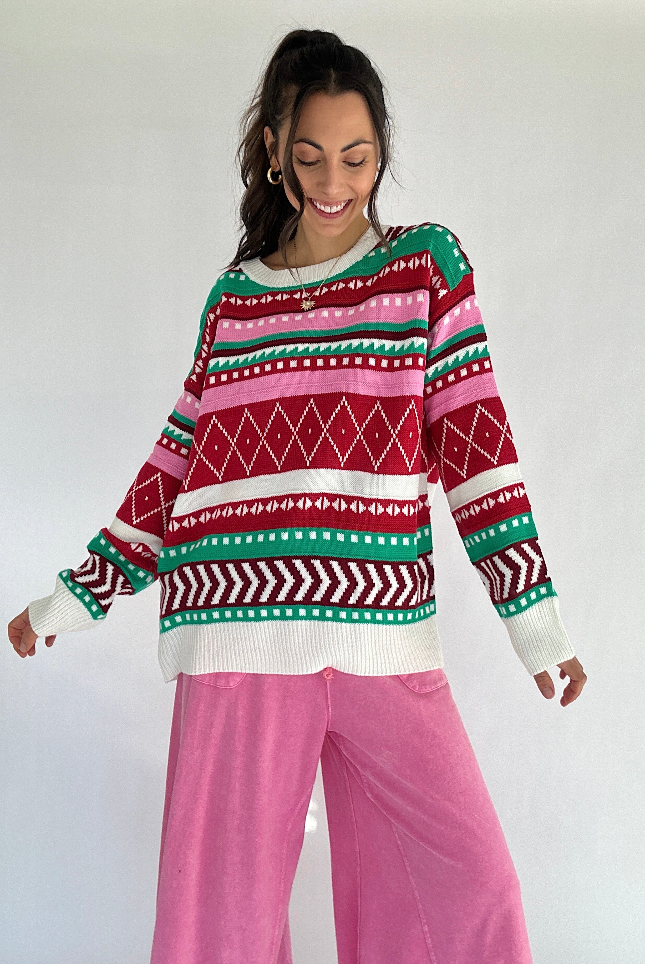 Person wearing a pink and red toned colorful patterned striped sweater and pink pants on a white background
