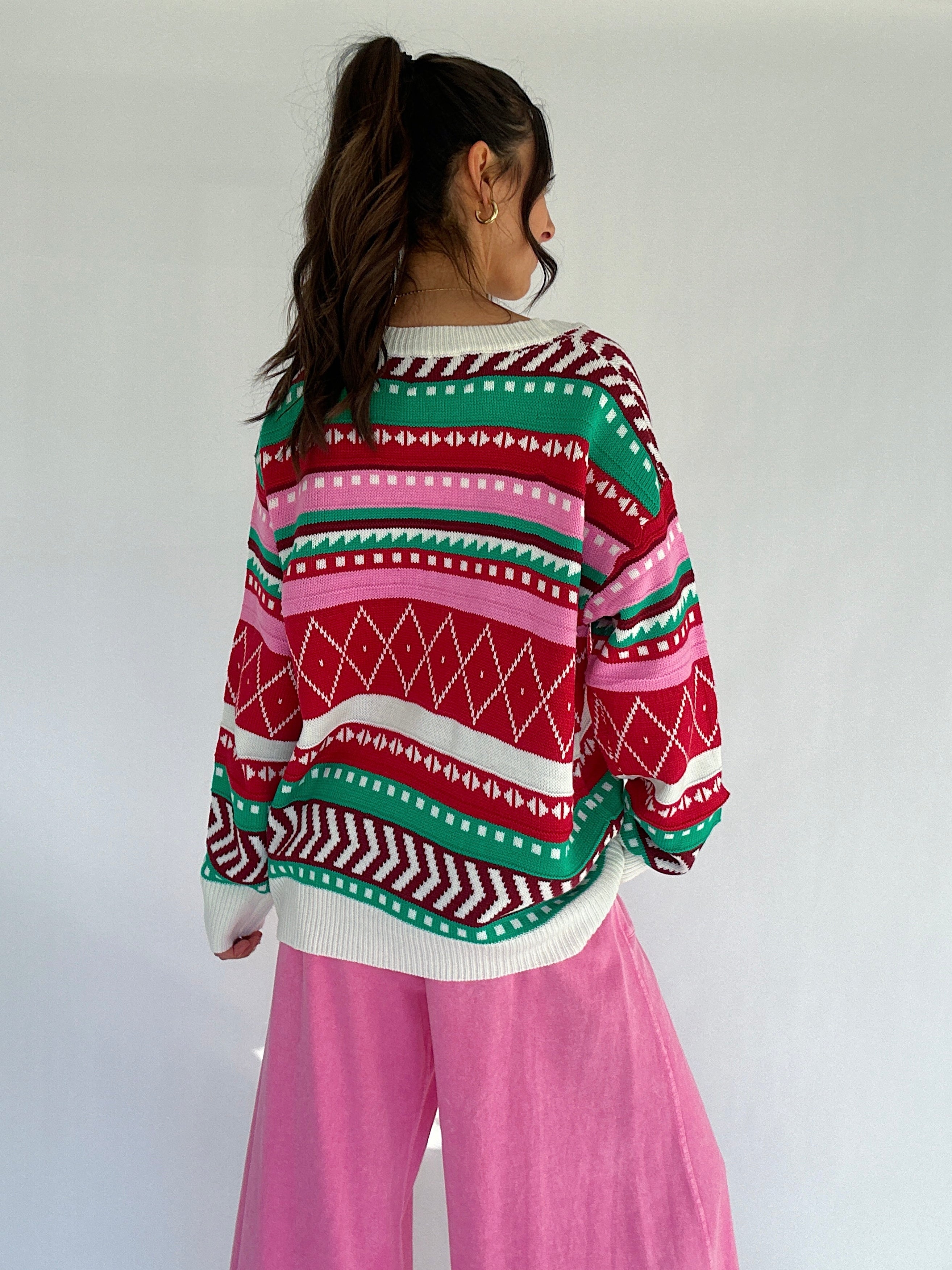 Person wearing a colorful patterned striped sweater with pink pants against a white background