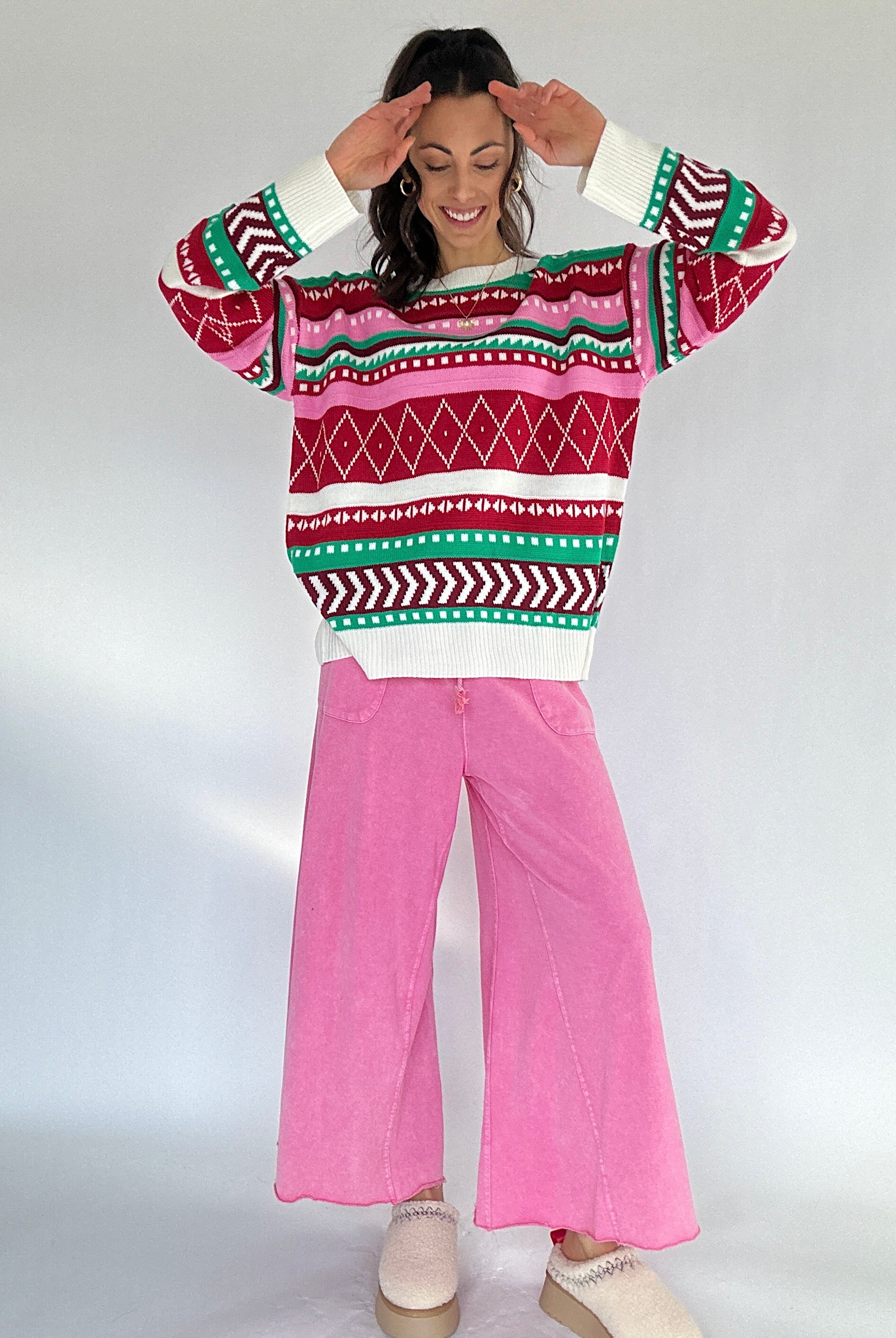 Person wearing a colorful patterned sweater and pink pants on a white background