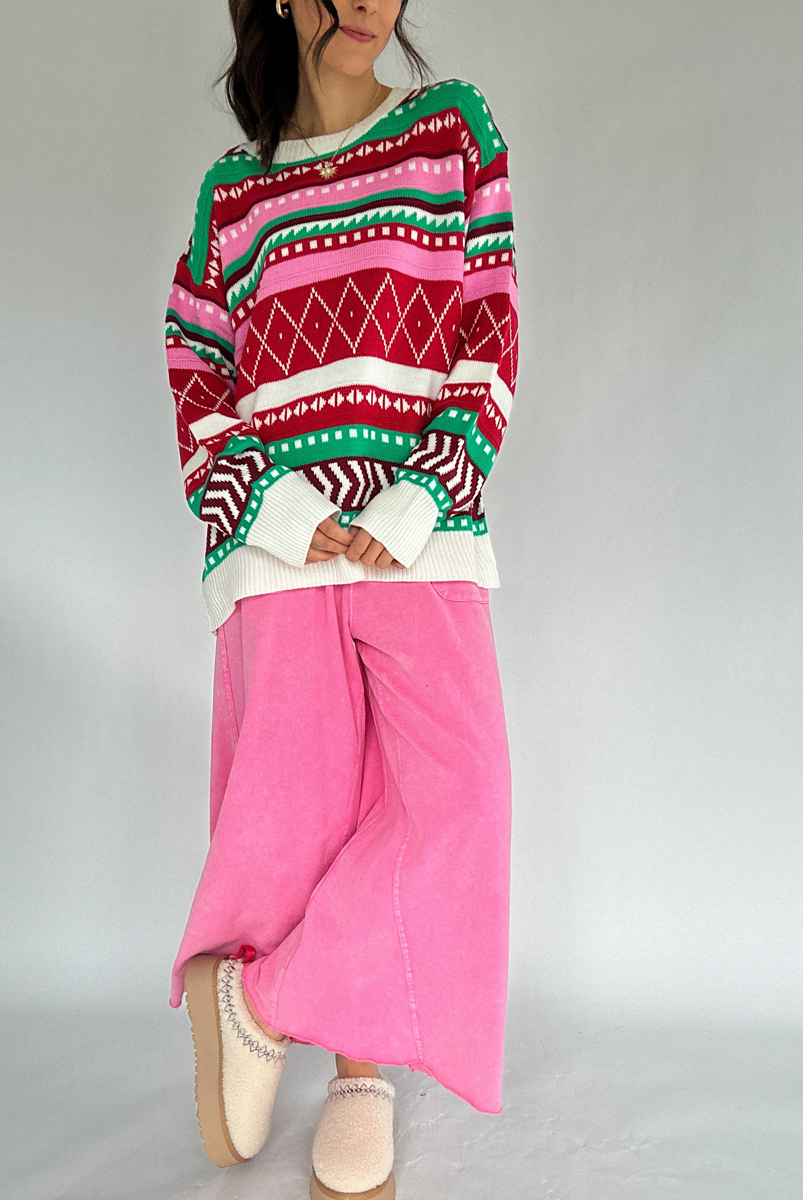 Person wearing a colorful patterned sweater and pink pants on a plain background