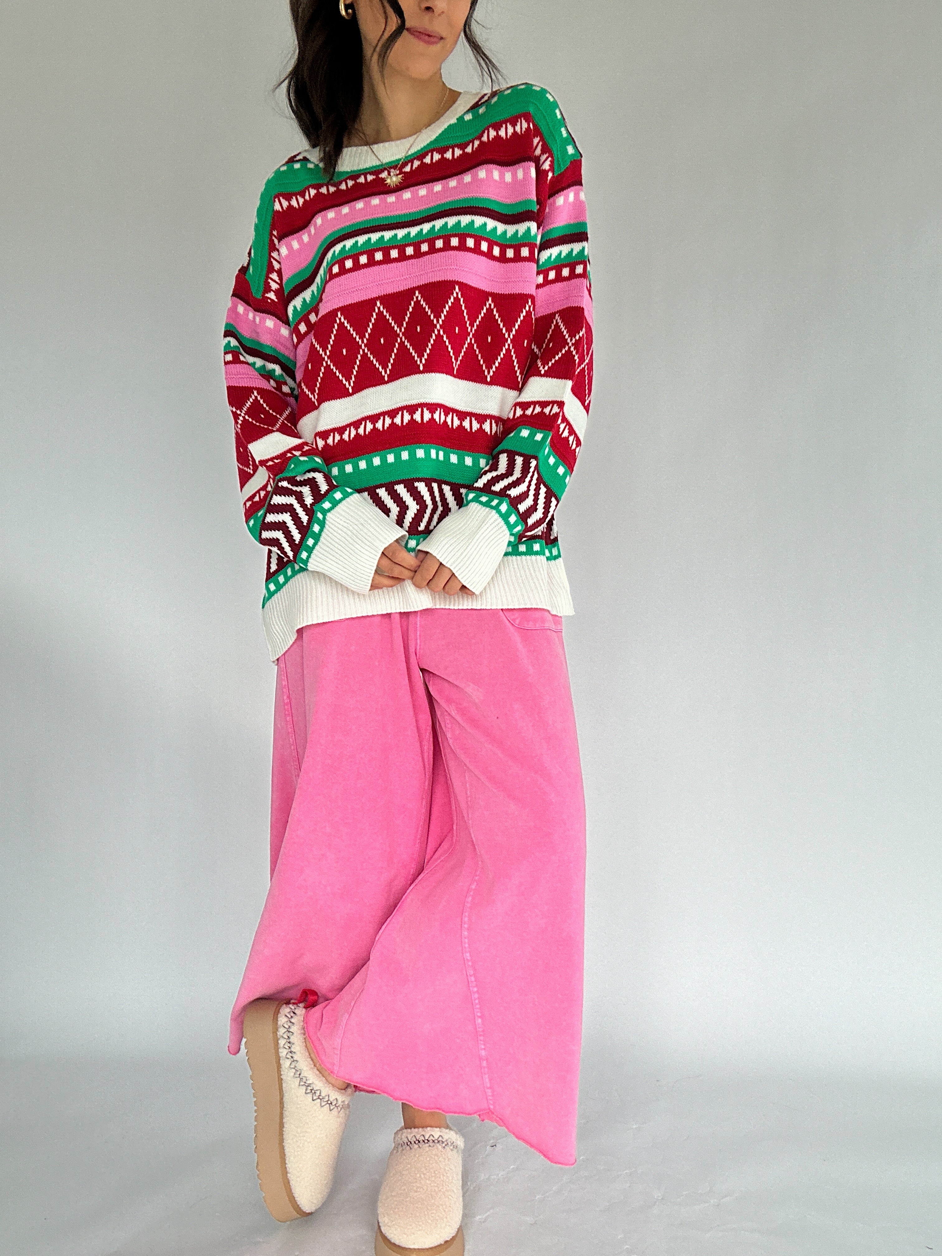 Person wearing a colorful patterned sweater and pink pants on a plain background