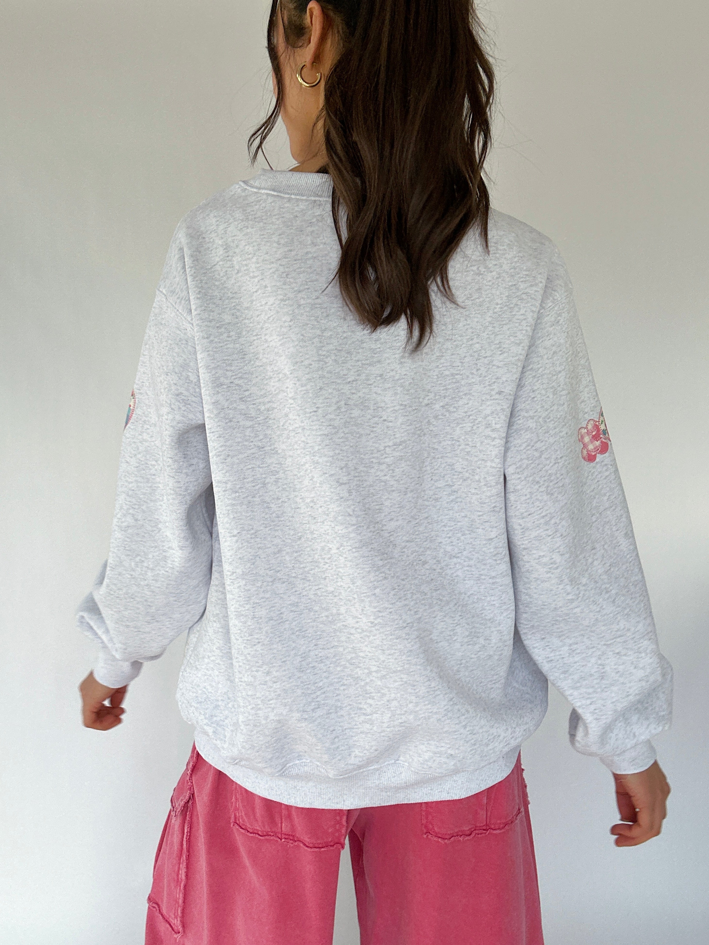 Person wearing a gray sweatshirt with a patch on the sleeve against a white background showing the back