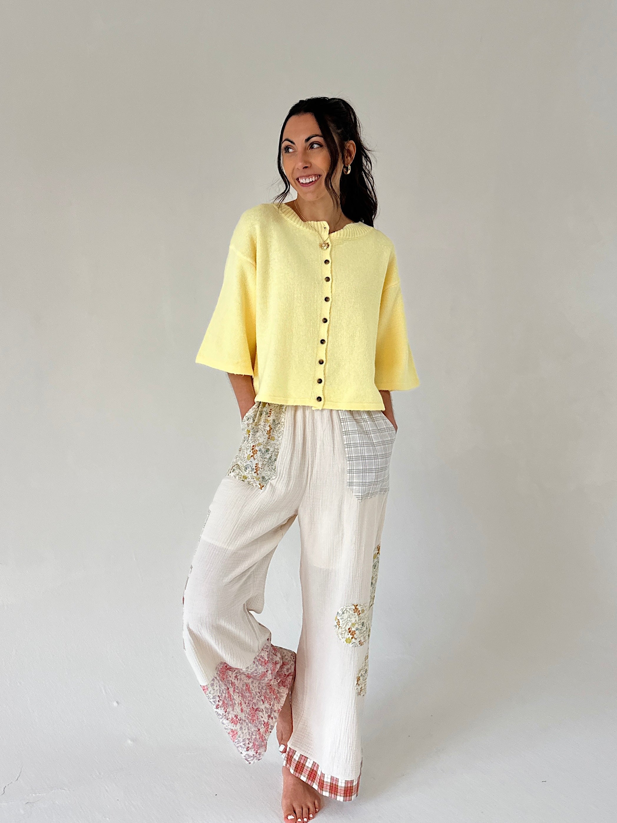 Woman wearing a yellow top and white pants with lace details on a plain background