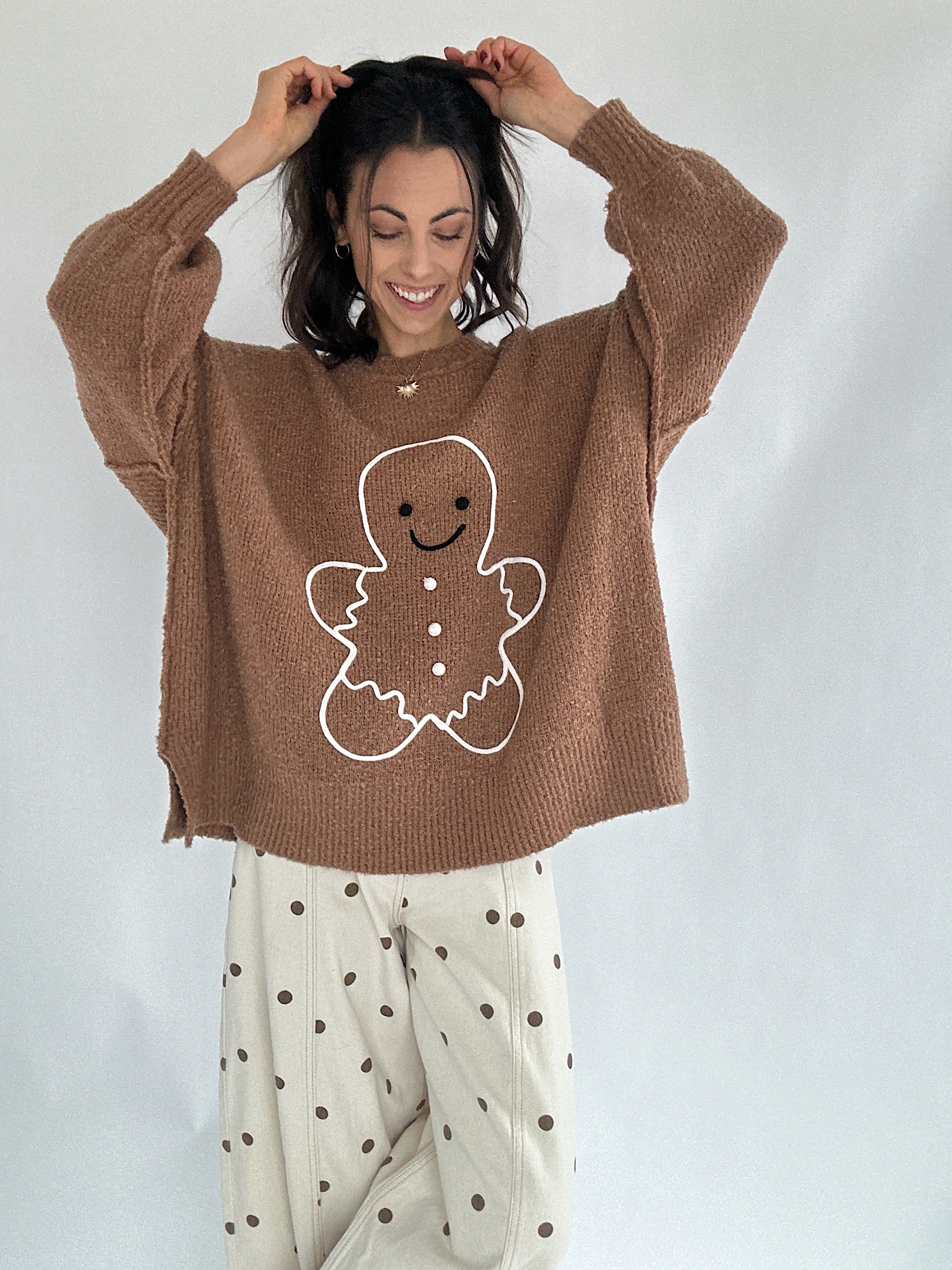 Person wearing a brown sweater with a gingerbread man design on a plain background with polka dot pants