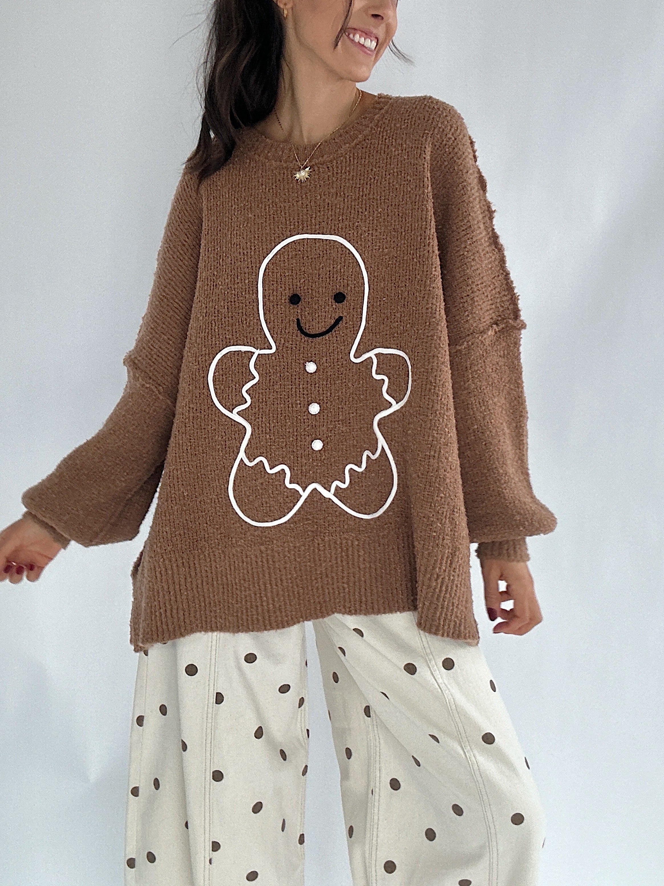 Person wearing a brown sweater with a gingerbread man design on a plain background and polka dot pants