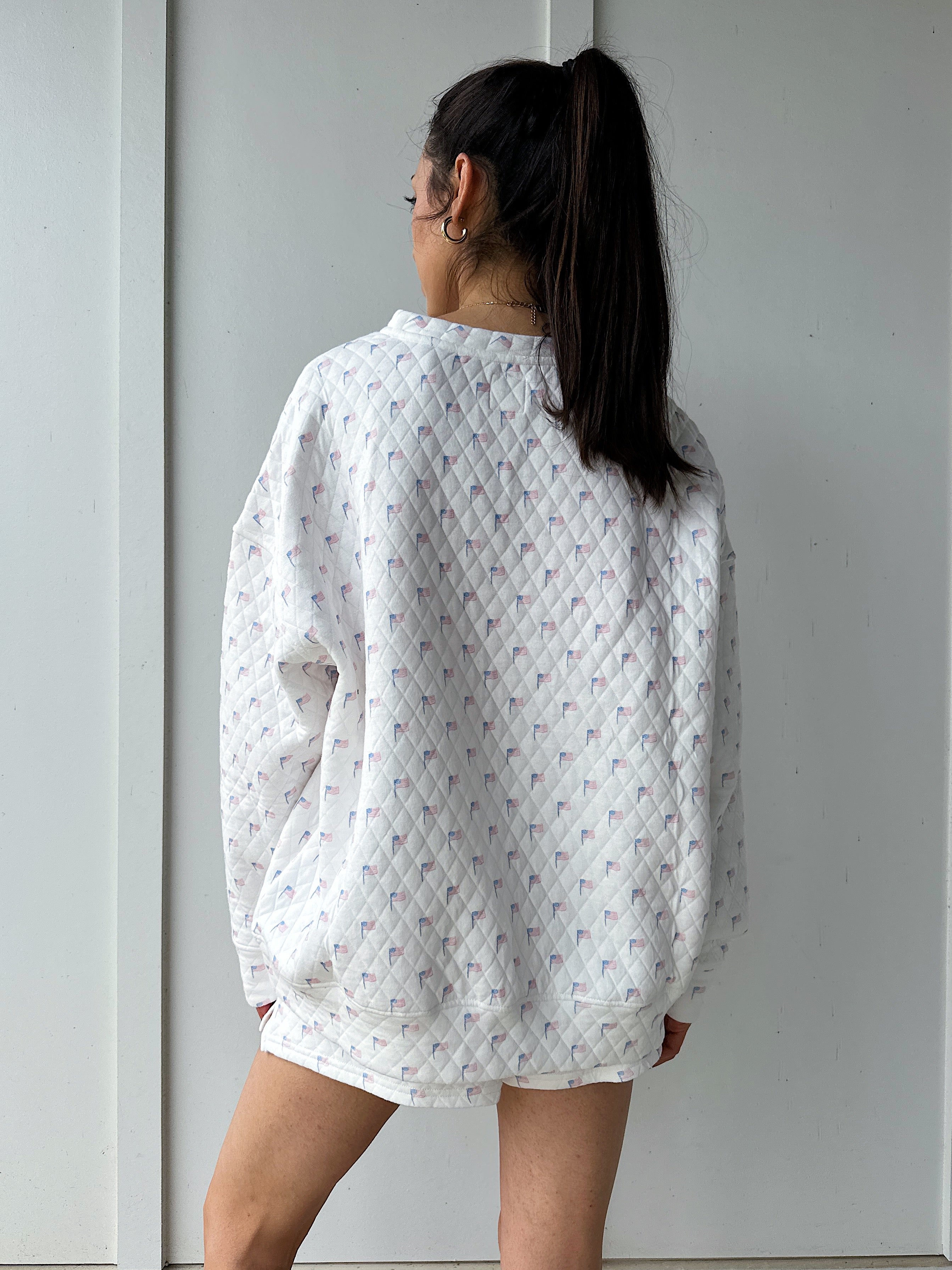 Person wearing a white quilted flag patterned sweatshirt against a plain background