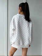 Person wearing a white quilted flag patterned sweatshirt against a plain background