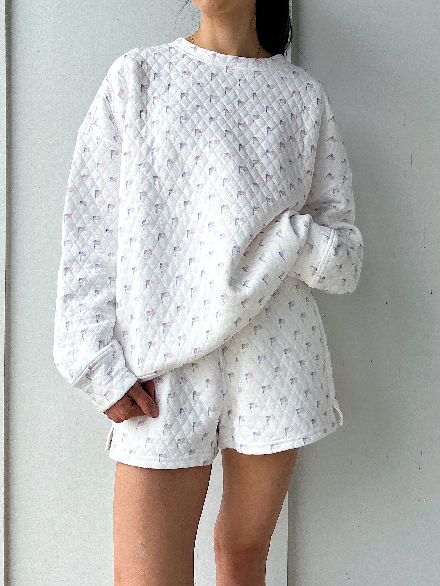 Person wearing a white quilted flag sweatshirt against a plain background
