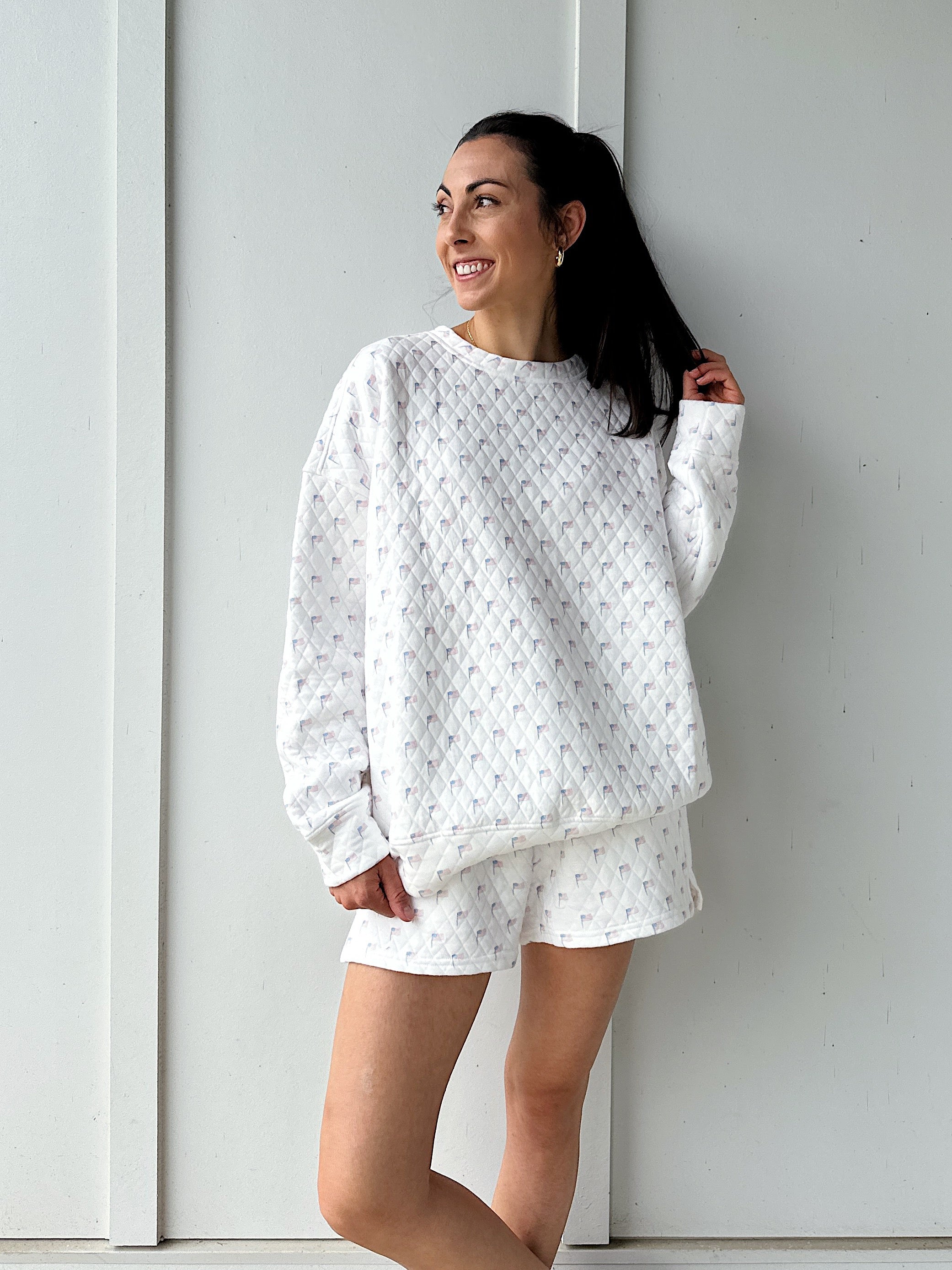 Woman wearing a white quilted flag patterned sweatshirt against a plain background
