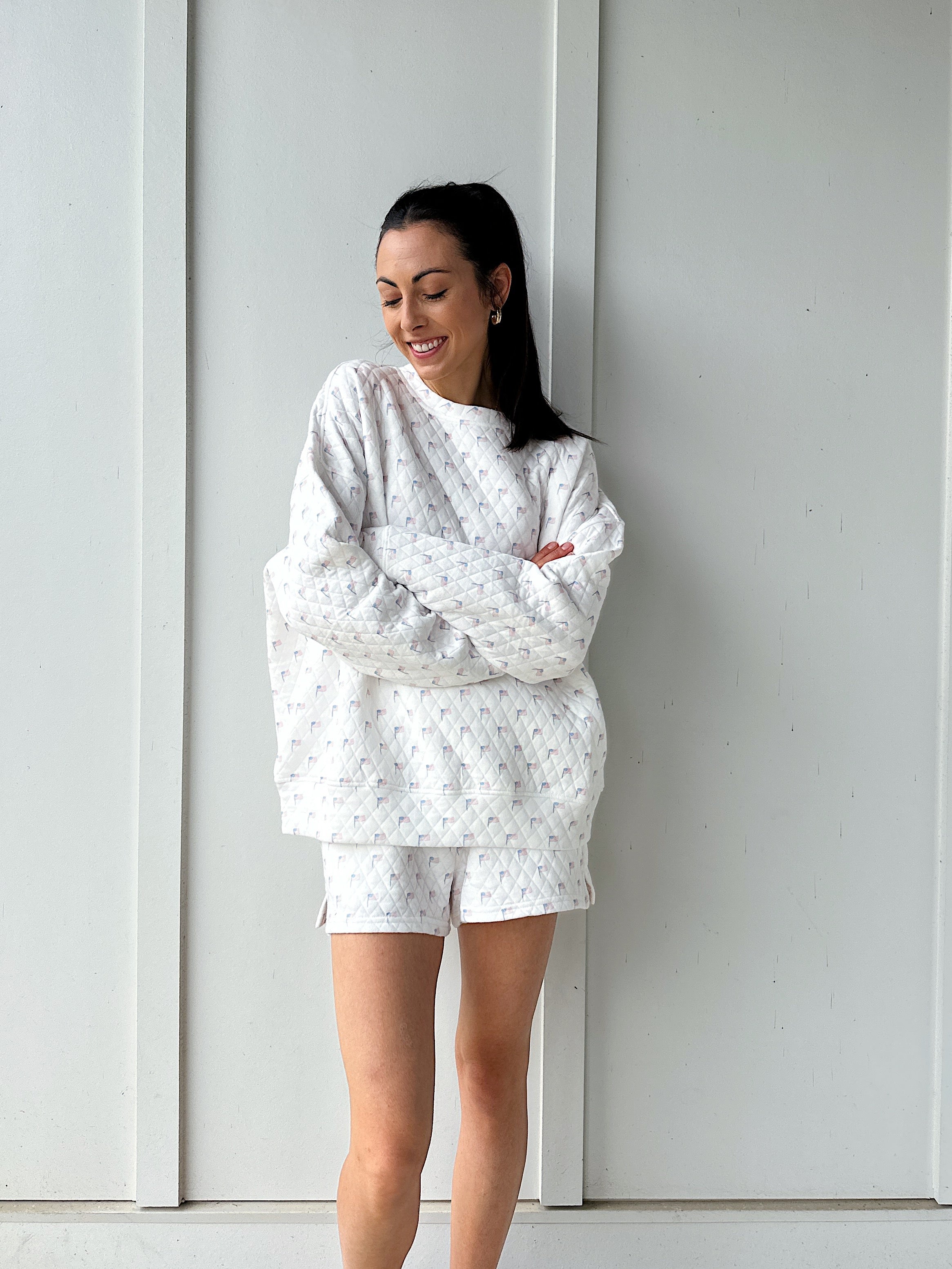 Woman wearing a white quilted flag patterned outfit standing against a white wall.
