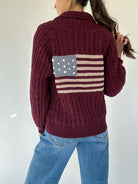 Person wearing a chenille maroon sweater with an American flag design on the back against a white background